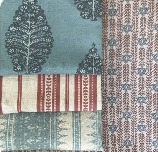 Close-up of folded fabric with various patterns, including teal with white trees, beige with red stripes, and light blue with white geometric designs.