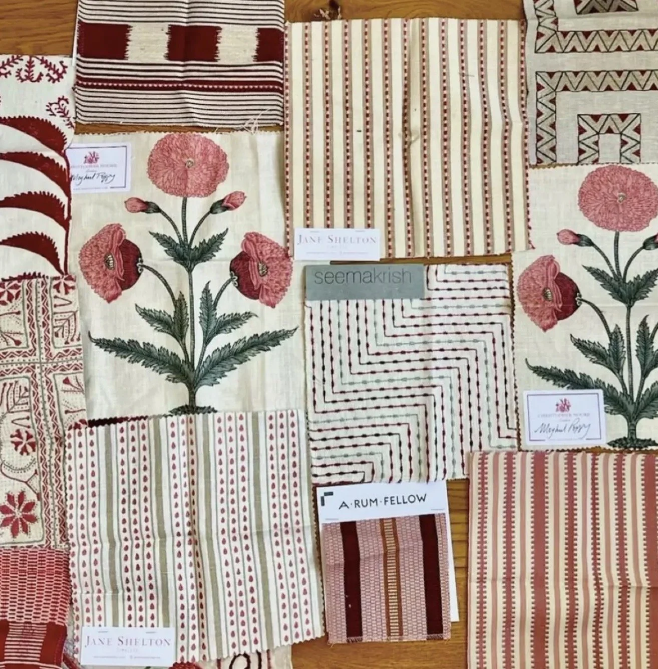 A collection of fabric swatches with various red, white, and beige patterns, including floral, striped, and geometric designs, labeled with designer names such as Jane Shelton, Seemakrish, and A Rum Fellow.