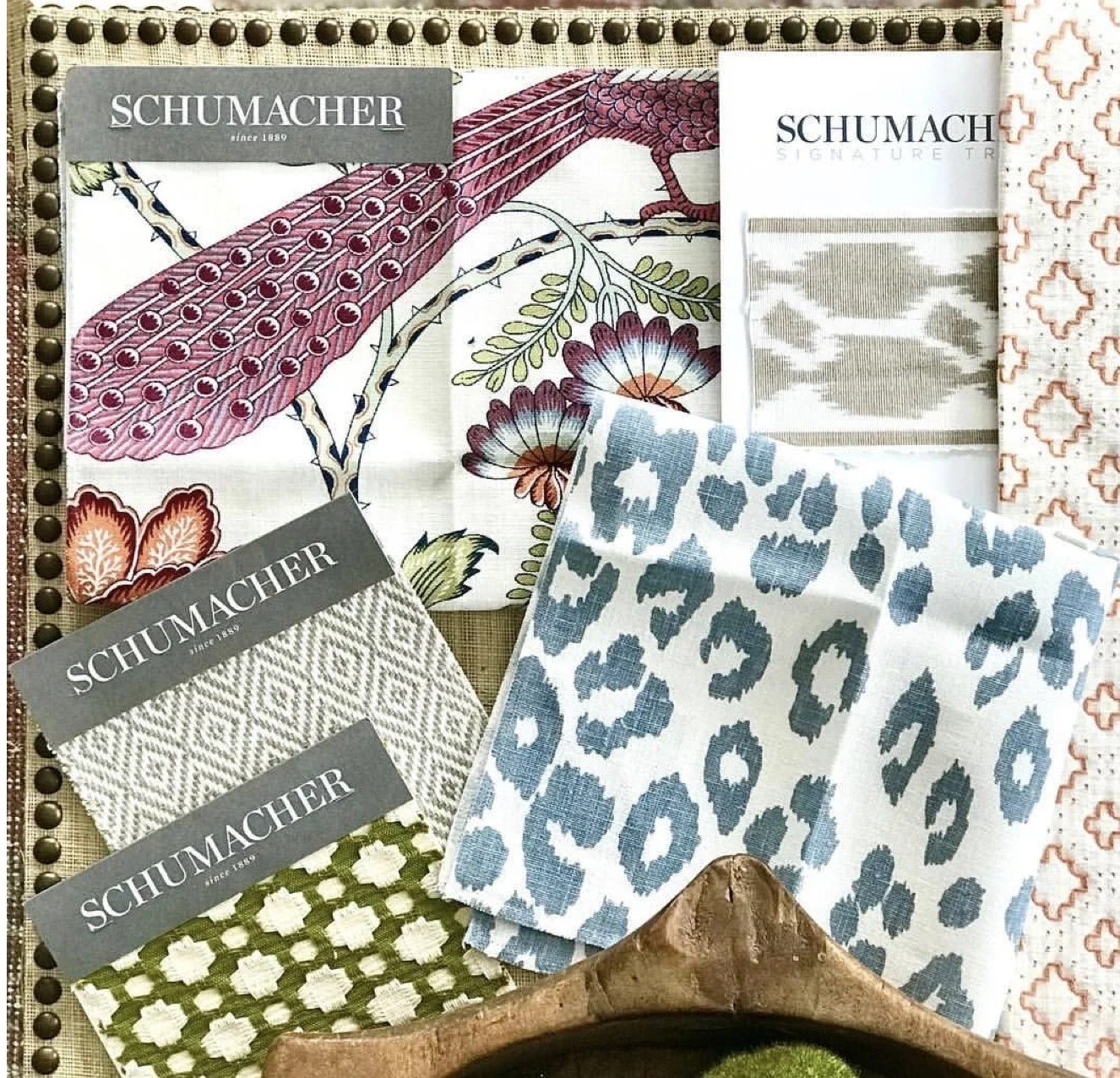 Display of various fabric samples with floral, animal print, and geometric patterns, along with Schumacher branded tags, arranged on a textured surface.