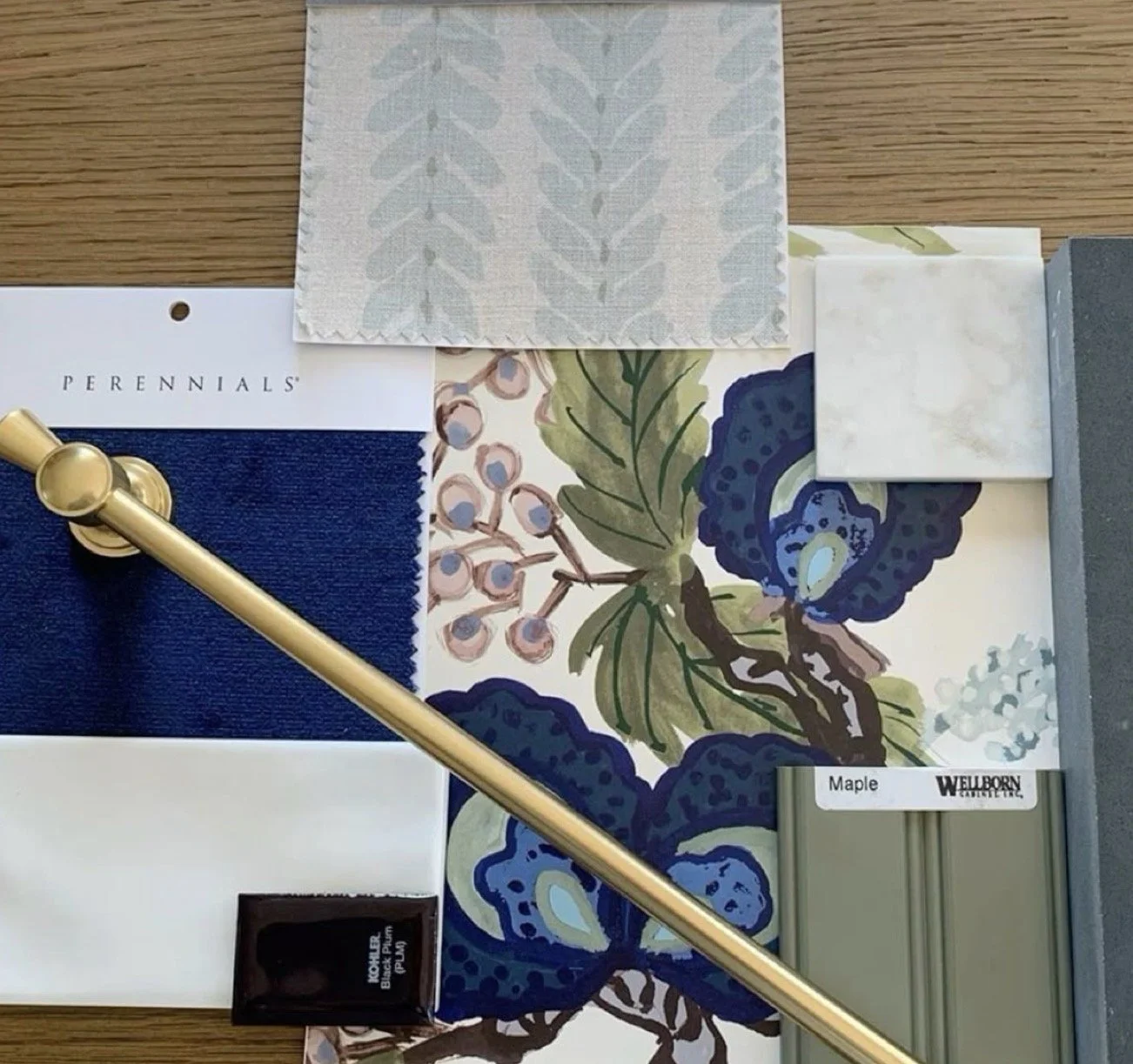 An assortment of paint, fabric, and tile samples on a wooden surface, including fabric swatches in blue, white, and gray, a painted floral pattern with blue and green, and small tiles in marble and concrete tones.