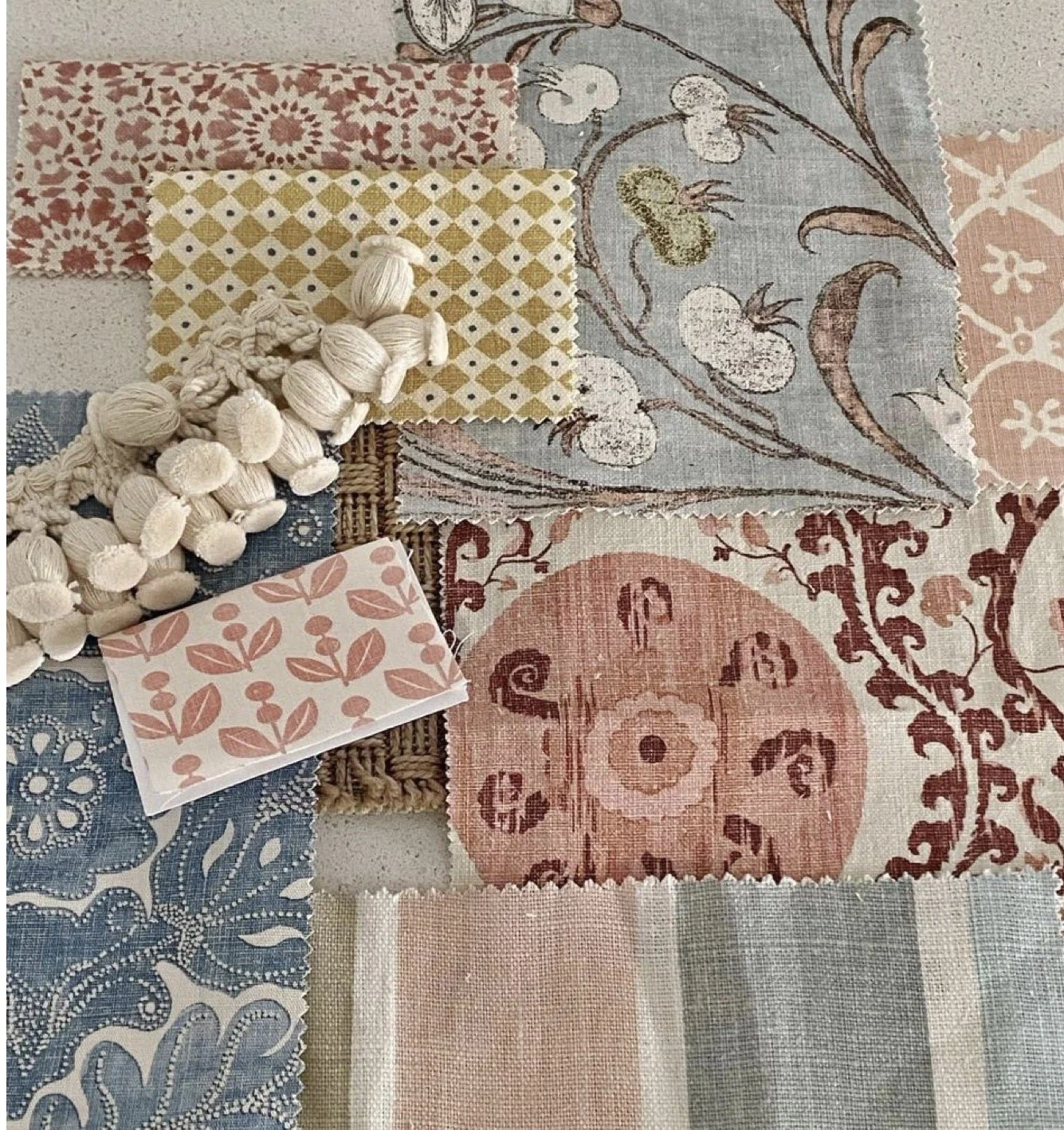 A collection of fabric swatches with various patterns and colors, including floral, geometric, and intricate designs. Some swatches are layered, and there's a white tassel trim on one swatch.