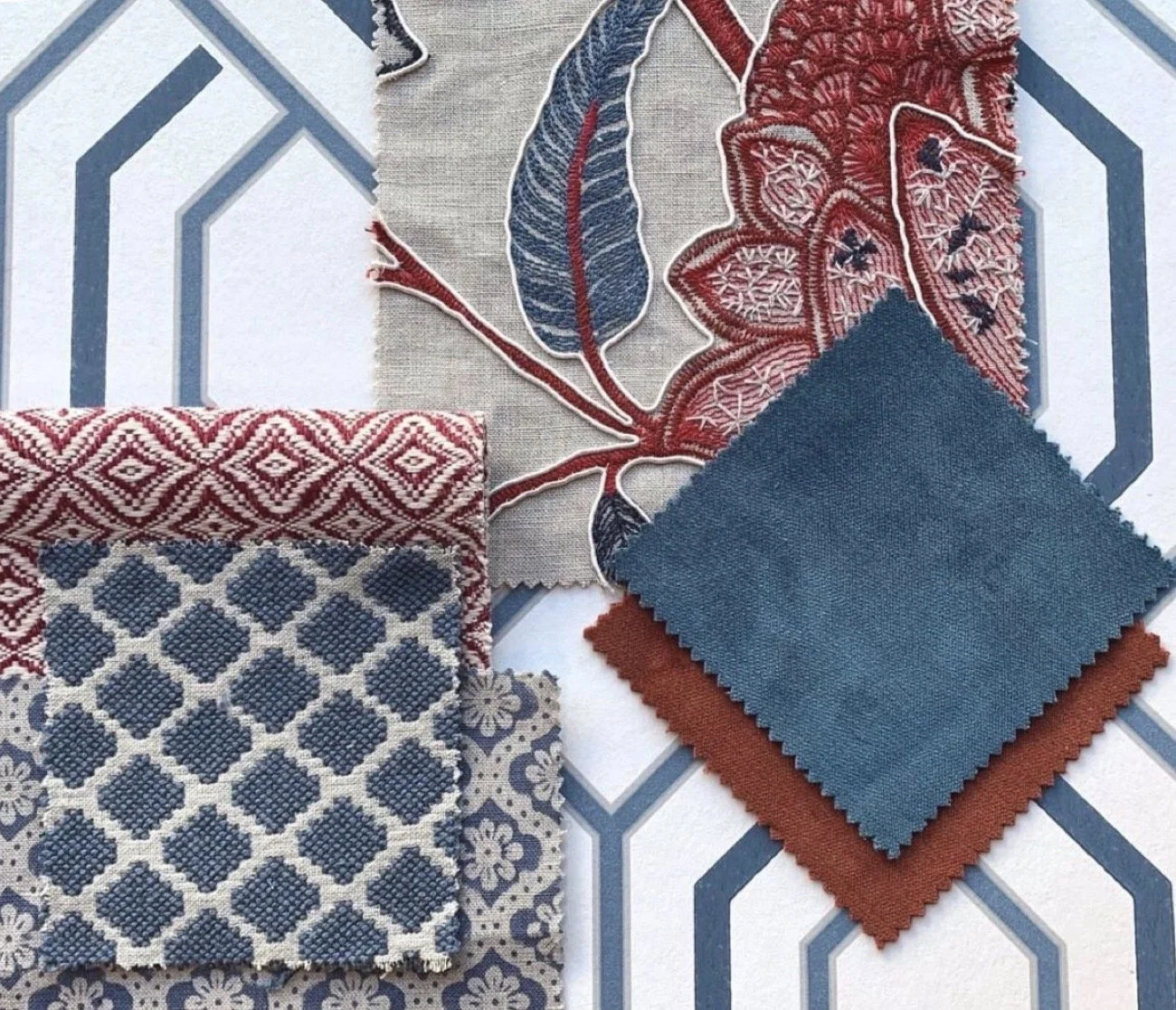 Fabric swatches with various patterns and textures, including floral and geometric designs in red, navy blue, beige, and white, laid out on a blue and white geometric tile surface.