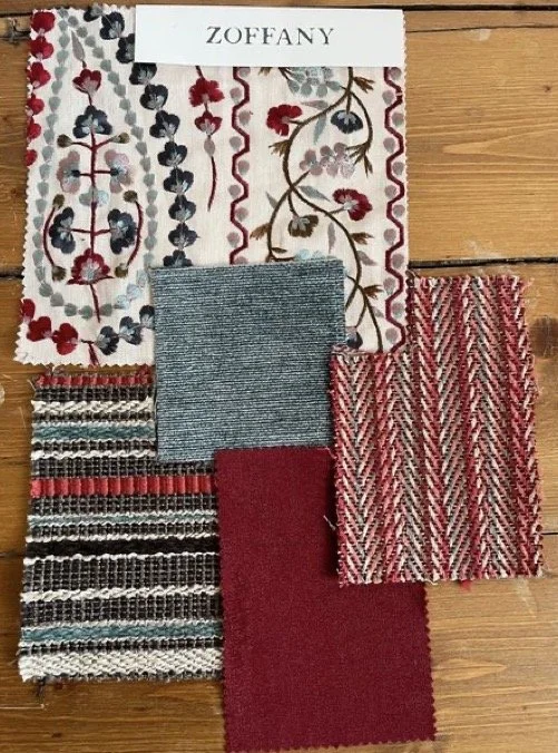 A collection of fabric swatches with various patterns and colors, including floral, striped, textured, and solid red, arranged on a wooden surface with a Zoffany fabric sample at the top.