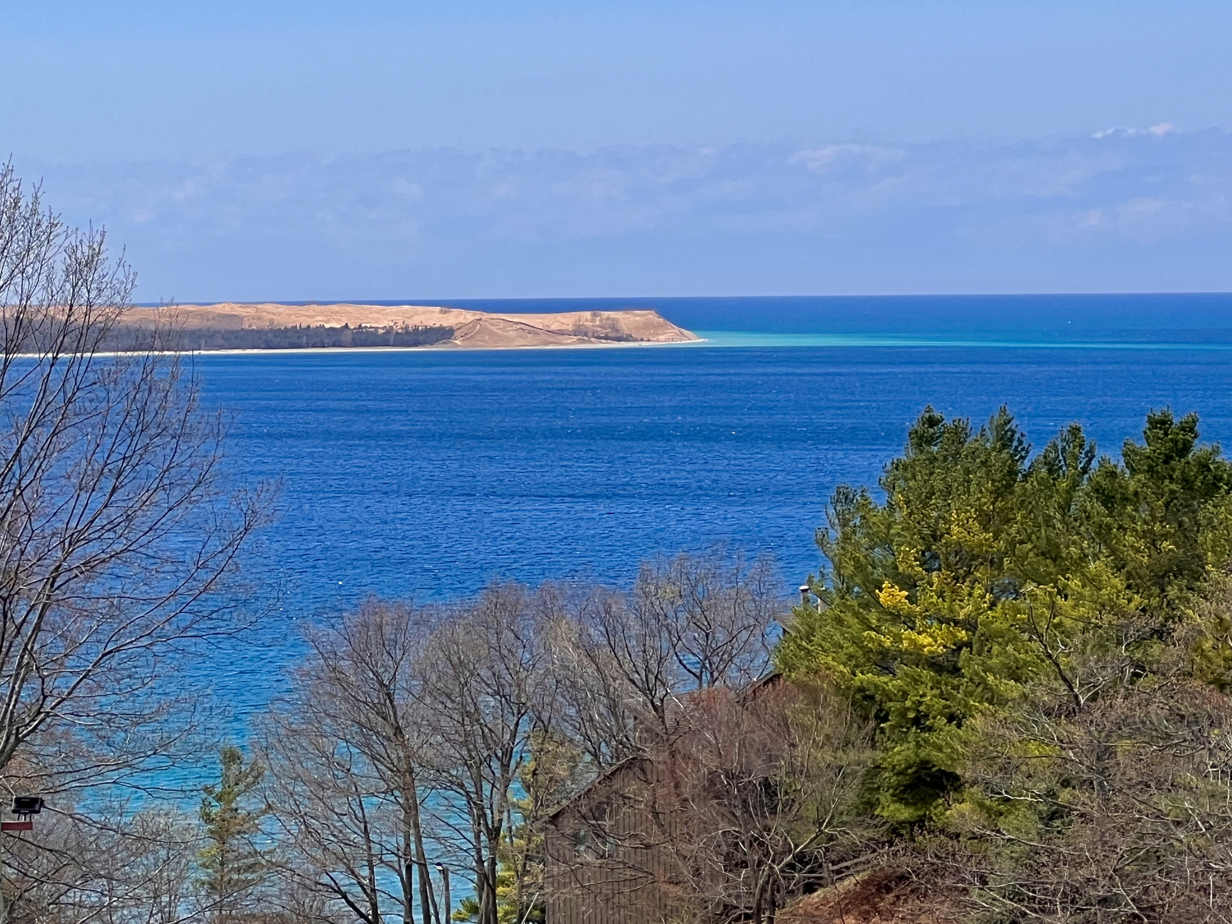 View of a large body of blue water with land and trees in the foreground and a distant shoreline on the horizon.