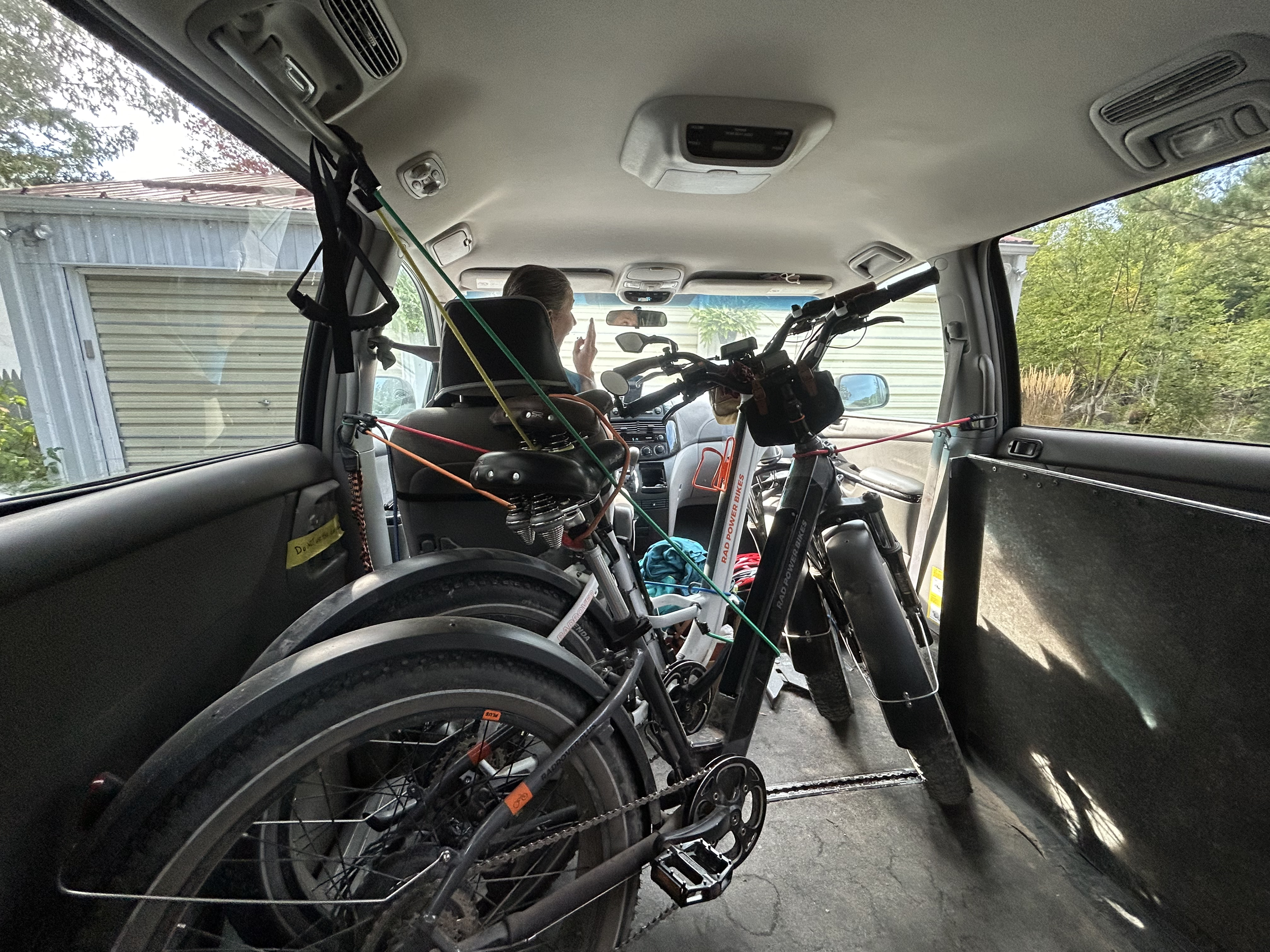 The interior of a vehicle with two electric bikes secured inside and a person sitting in the front passenger seat.