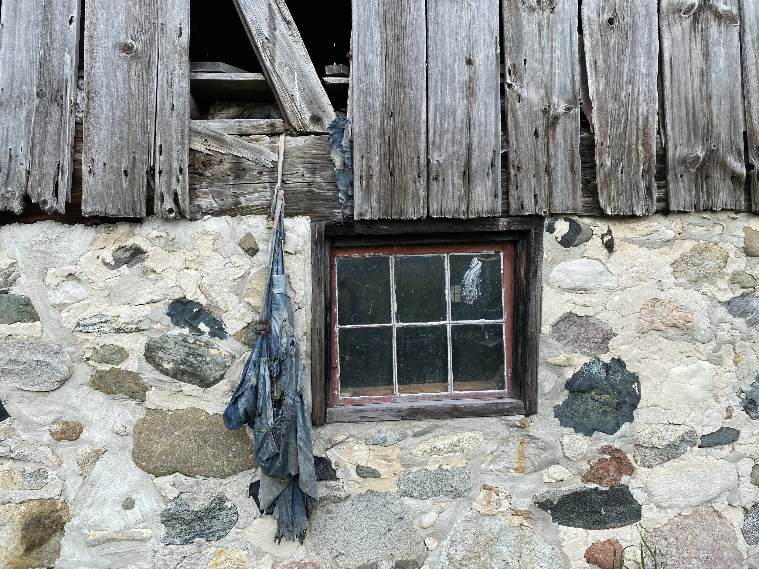 Close-up of an old, weathered stone and wood building with a broken window and tattered cloth hanging beside it.