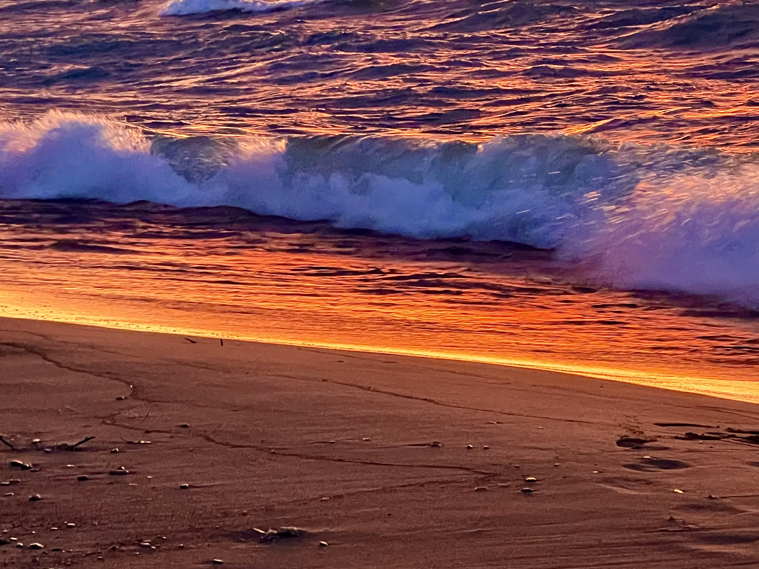 Sunset over the ocean with waves crashing onto a sandy beach.