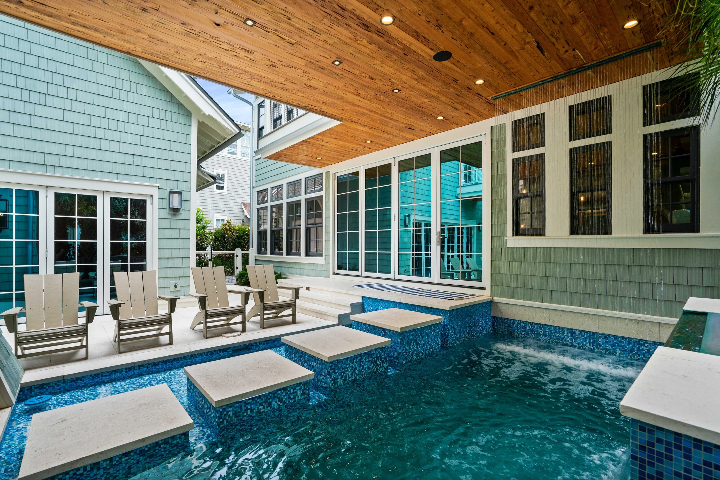 Outdoor patio area with a small pool, beige lounge chairs, and a wooden ceiling.
