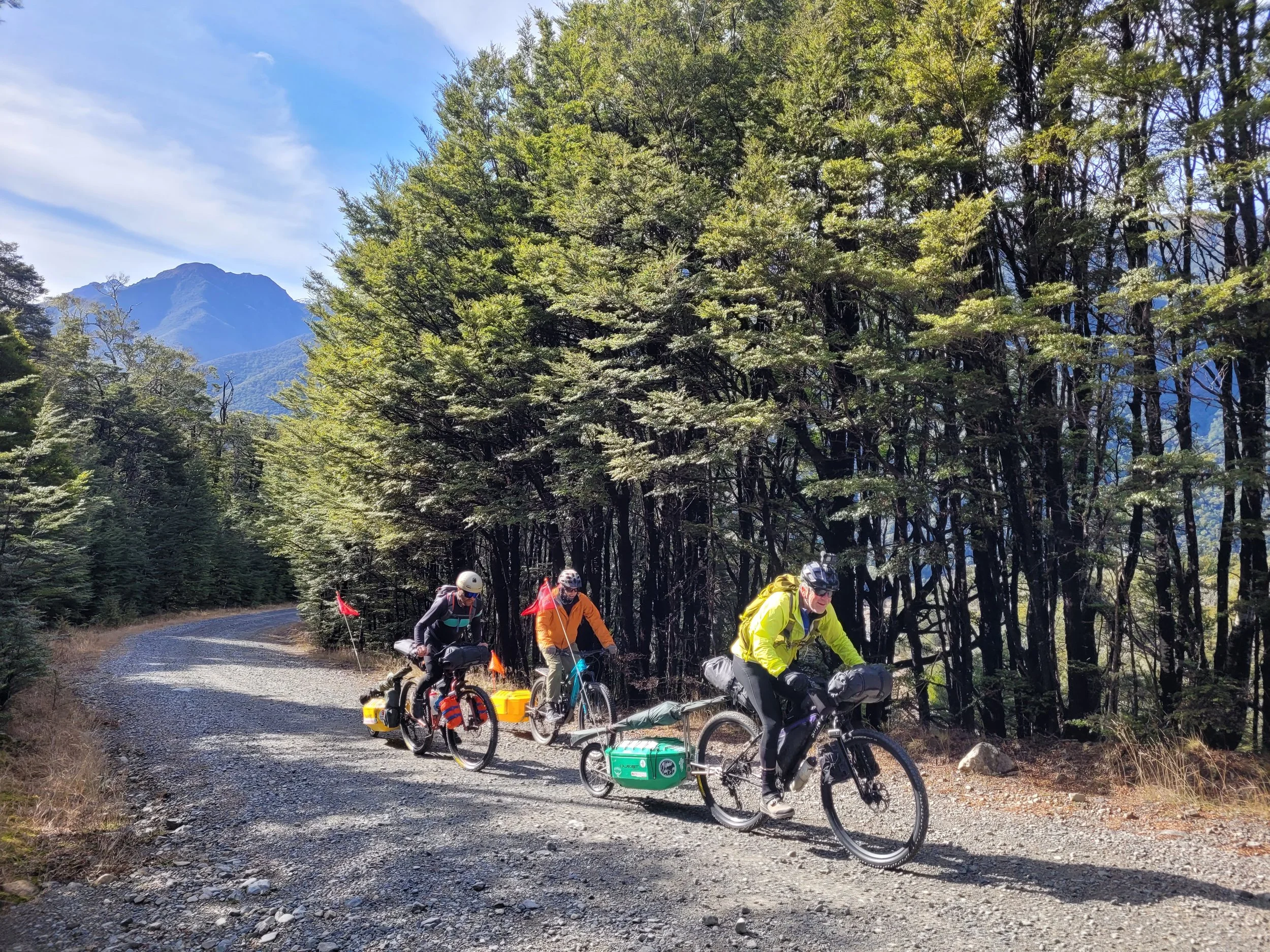 Three cyclists biking up a dirt road all towing a quest trailer behind them looking adventure ready