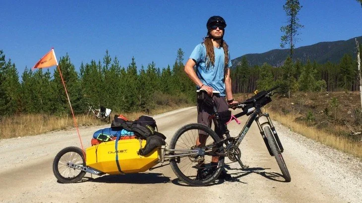 Owner and inventor Chris Harrington standing with his bike and quest trailer attached in the middle of a dirt road during an adventure
