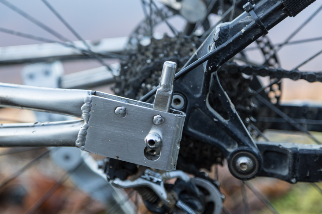 Close-up of a Quest bike trailer's rear derailleur and gear cassette, with a metal plate mounted on the frame.
