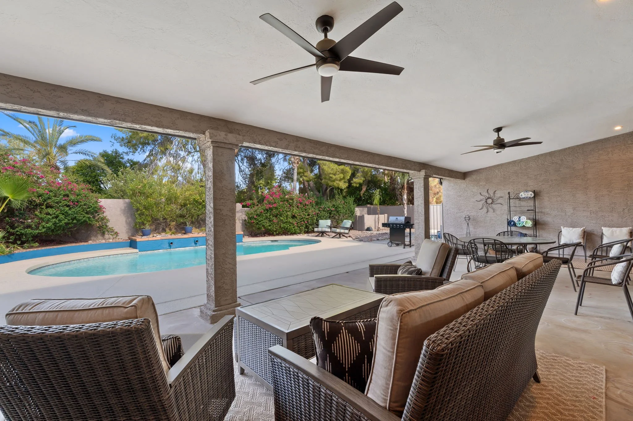 Covered patio with ceiling fans, outdoor seating, a table, a barbecue grill, and a view of a backyard with a swimming pool and landscaping.