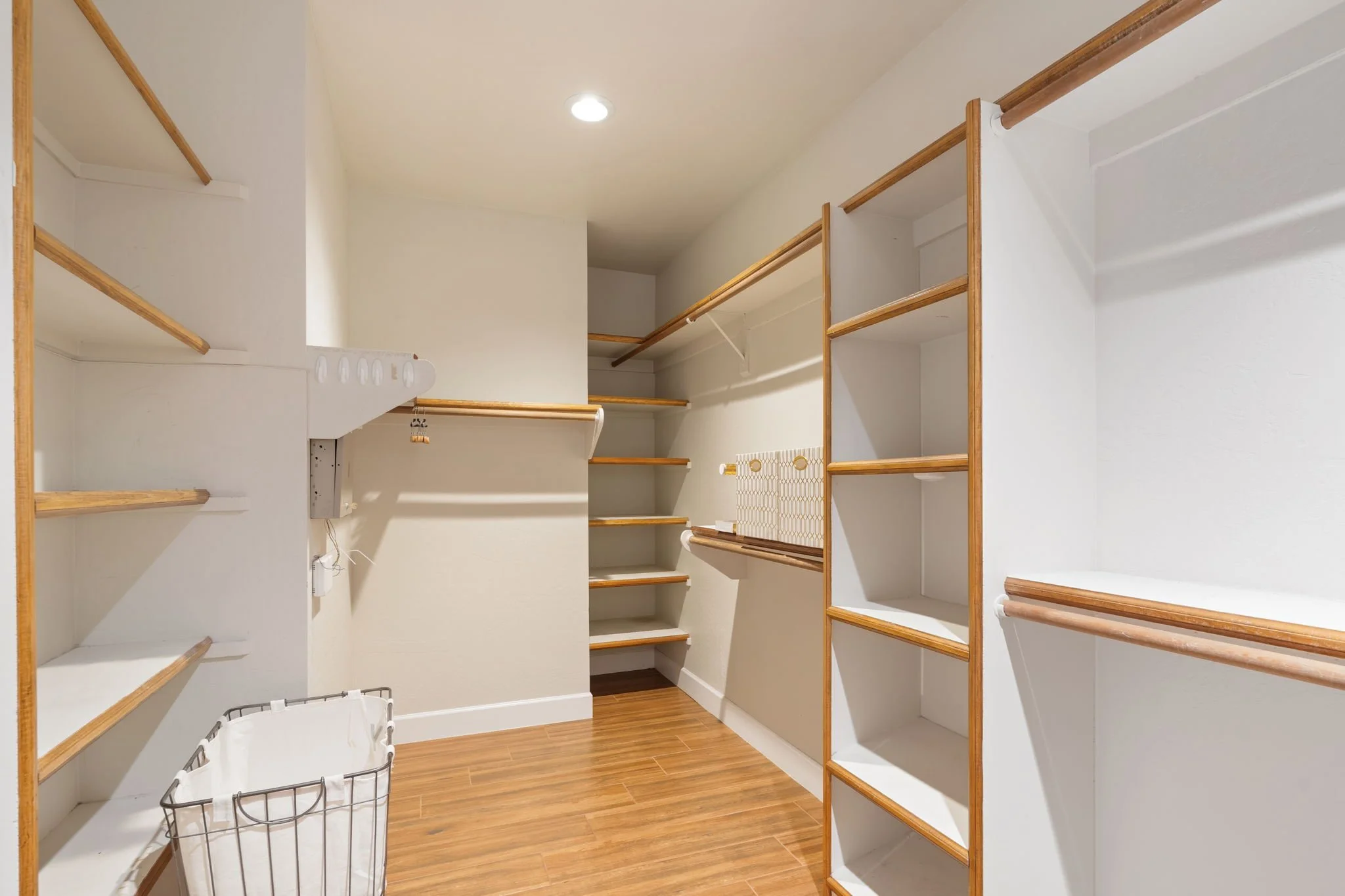 Walk-in closet with white walls, wooden shelves, and hanging rods available in primary suite.
