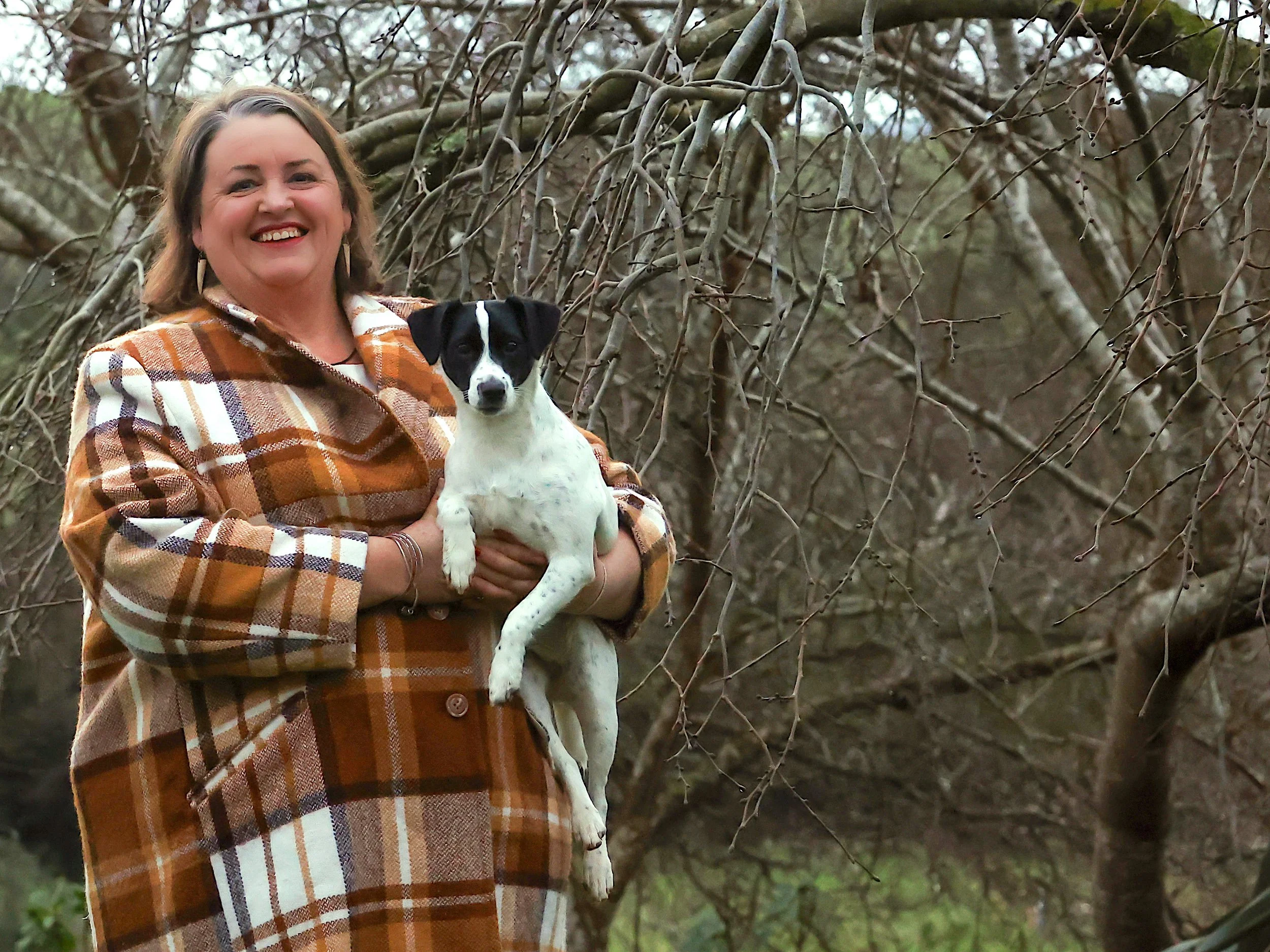 Angela smiles in her garden holding a small dog
