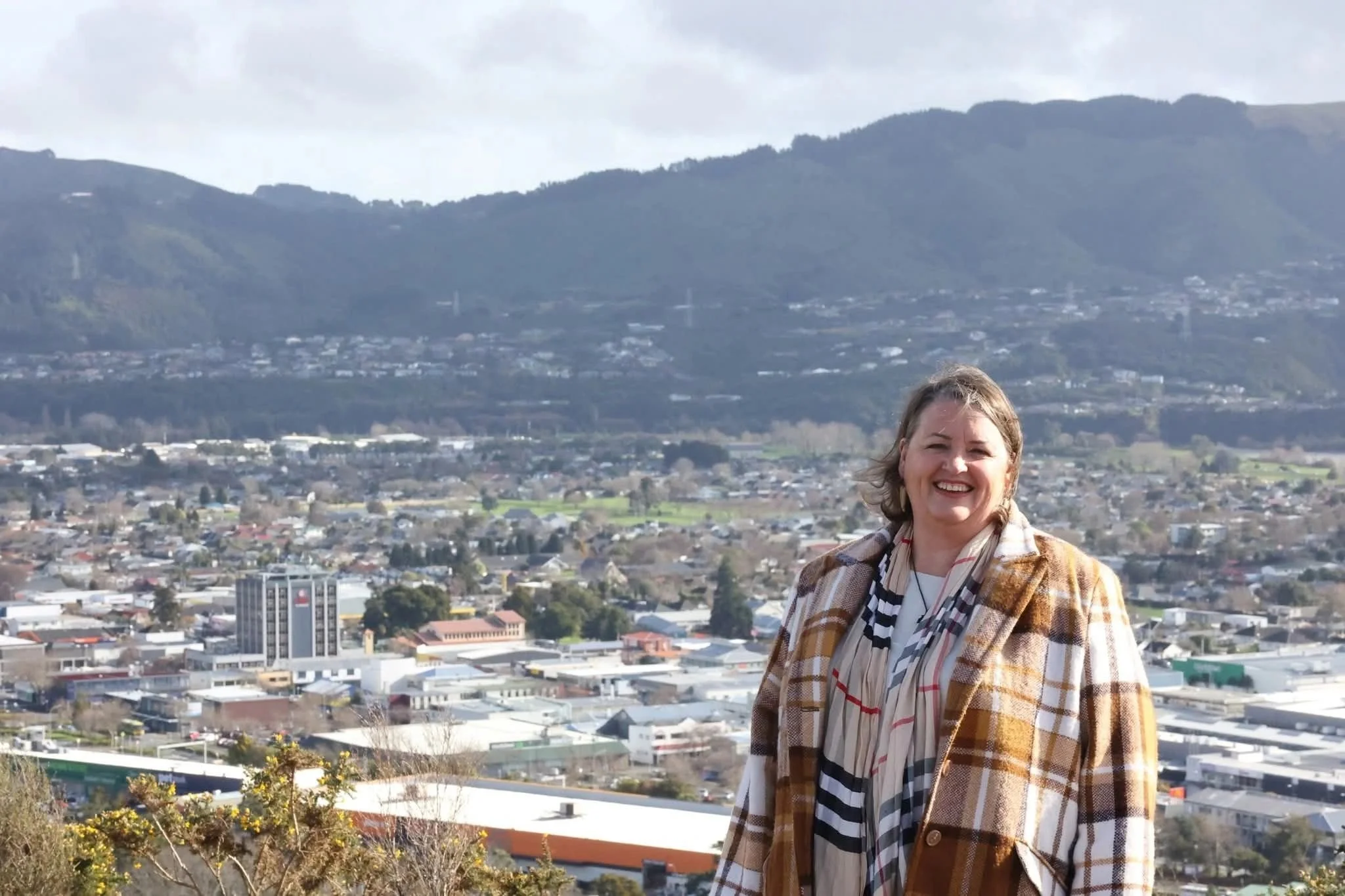 Angela smiles on hilltop with view of Upper Hutt behind her