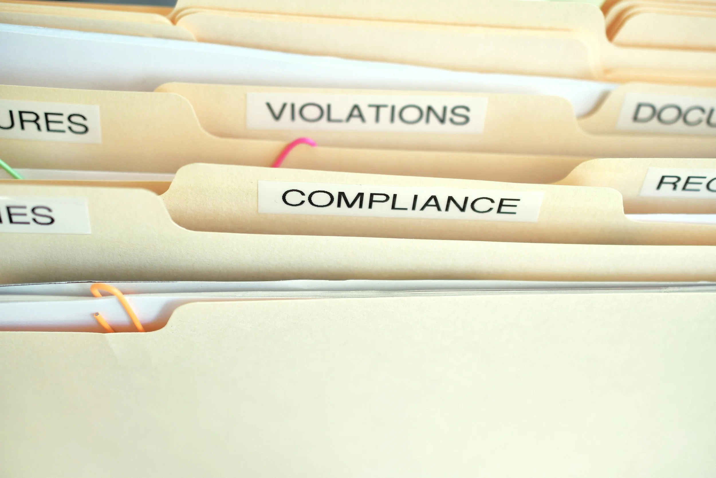 File folders labeled 'VIOLATIONS,' 'COMPLIANCE,' and 'DOCUMENTS' in a filing cabinet representing HOA warning letters. 