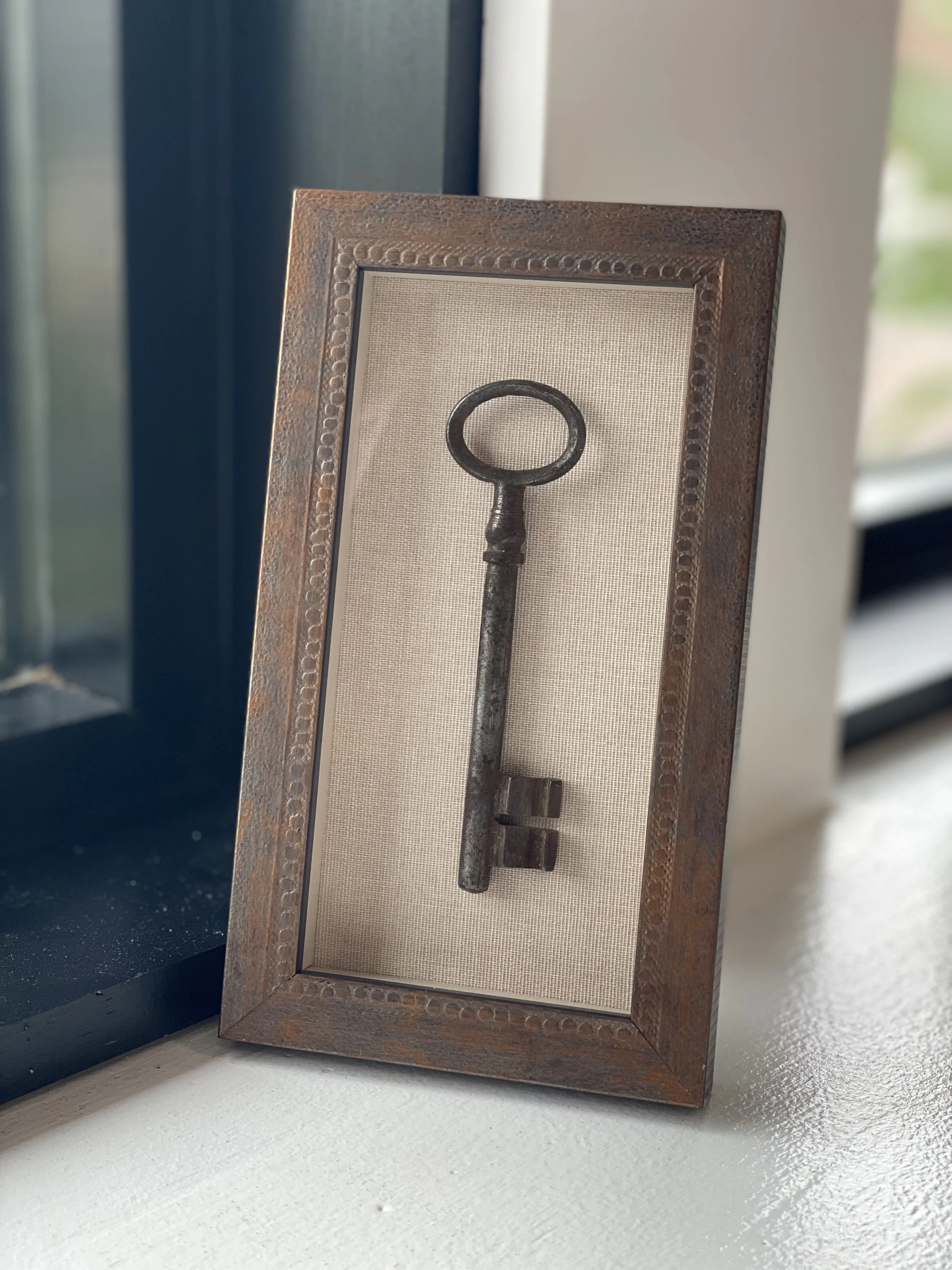 A framed decorative piece featuring an antique key on a beige background.