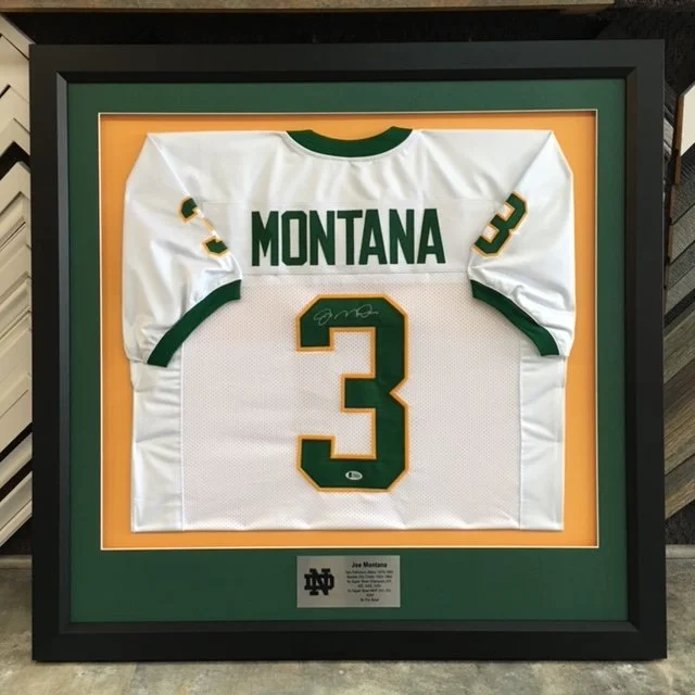Framed green and white football jersey with the name 'MONTANA' and the number 3, signed on the number, displayed against an orange background.