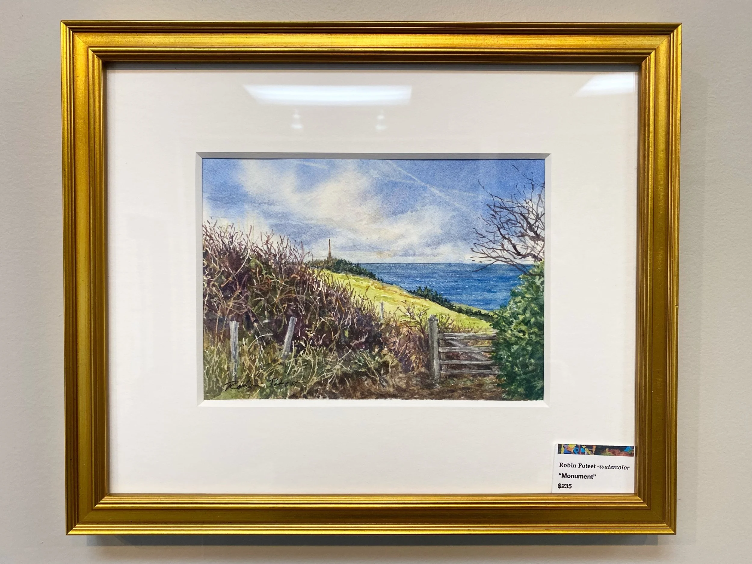 Watercolor painting of a landscape featuring trees, a fence, grassy hills, and a cloudy sky, in a gold frame.