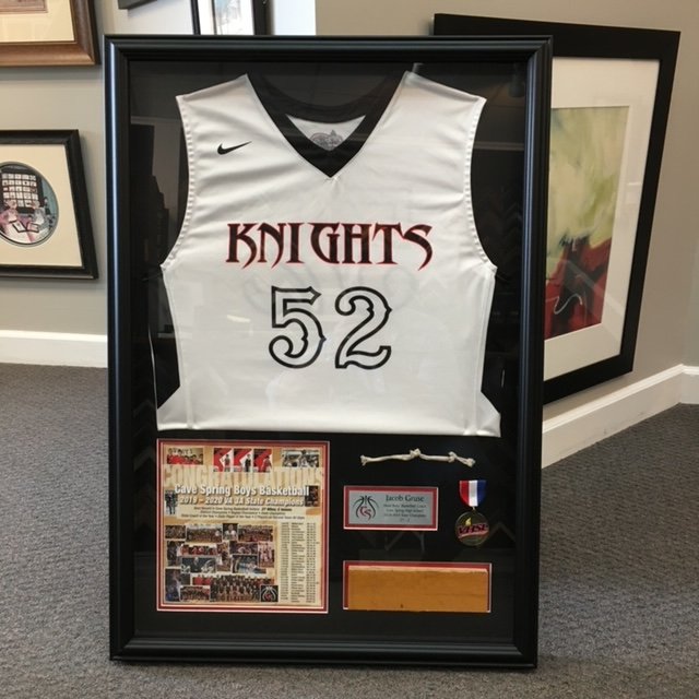 Framed sports jersey and memorabilia including a basketball jersey with the team name 'Knights' and the number 52, a newspaper clipping, a medal, a small plaque, and a small white object.