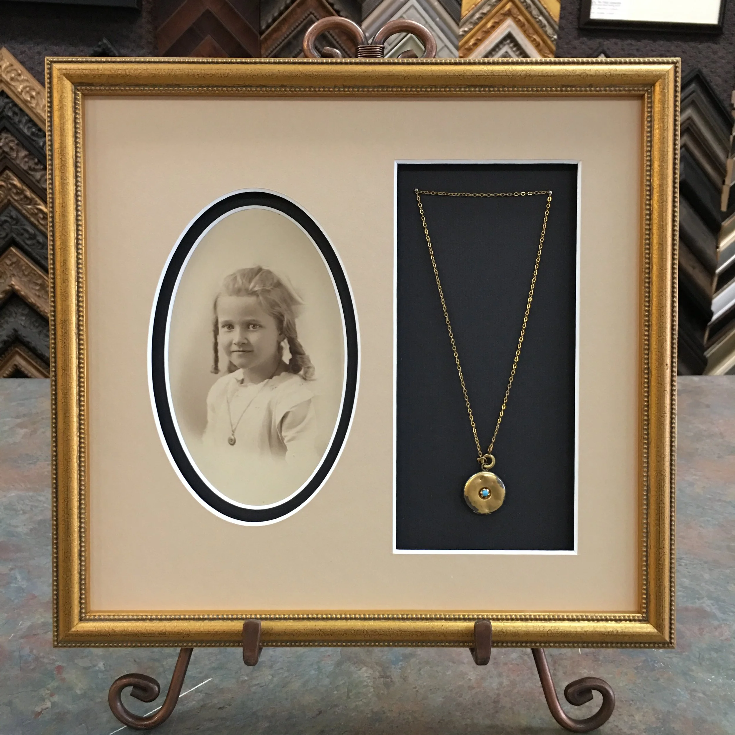 Display frame with various picture frames and jewelry on a stand in a framing shop.