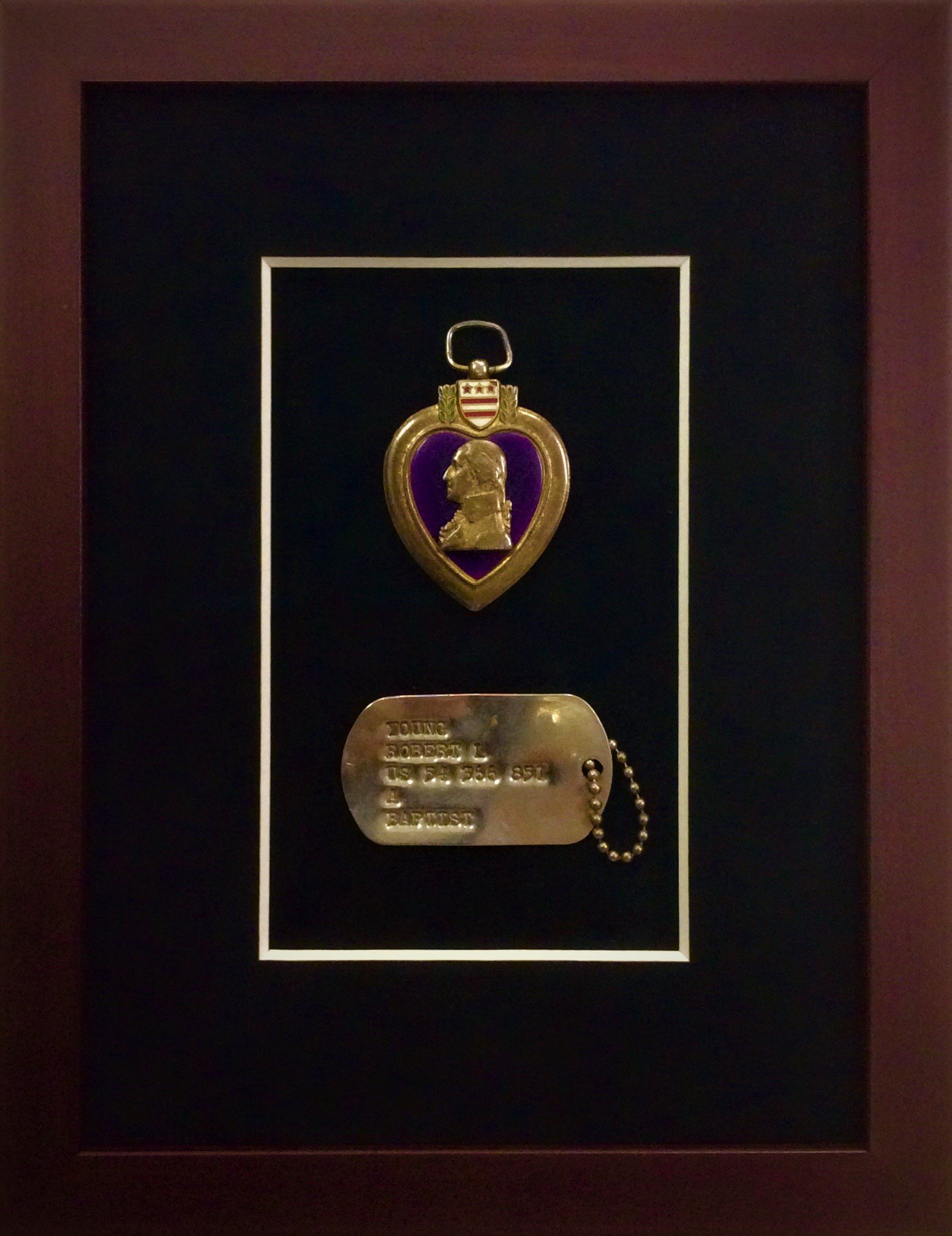 A military medal with a portrait in profile of a man, a shield with red and white stripes and three stars, and a purple background, displayed in a black display case with a gold date plate.