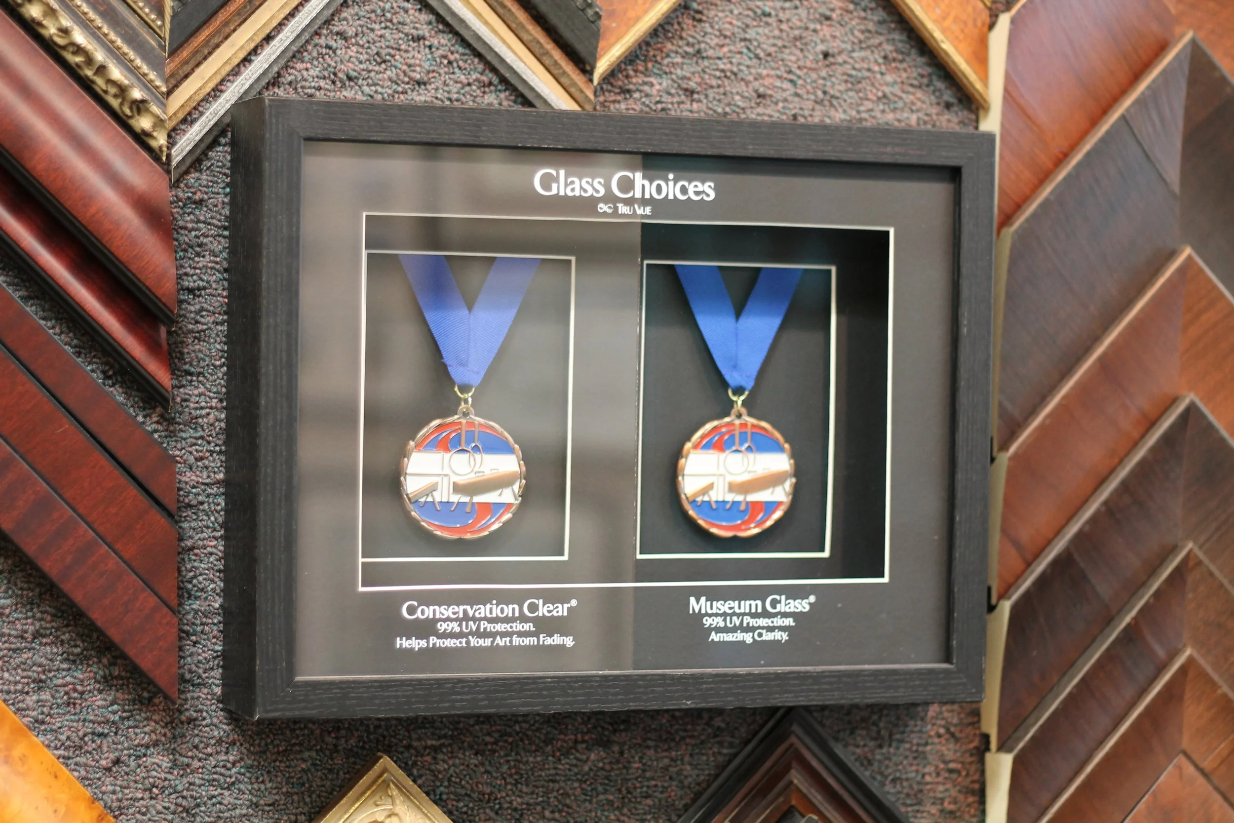 Display case with two medals hanging on blue ribbons, showcasing the artwork of a basketball hoop. The case is surrounded by various photo frame samples.