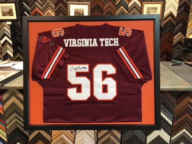 Framed Virginia Tech football jersey with number 56 and autograph, displayed against an orange background in a frame.