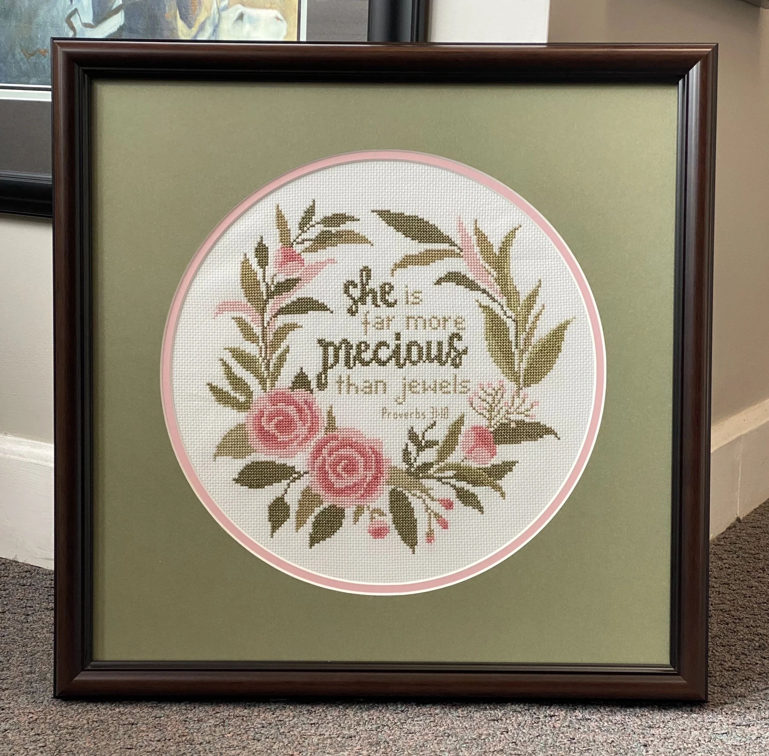 Framed cross-stitch embroidery with floral design and the words "she is far more precious".