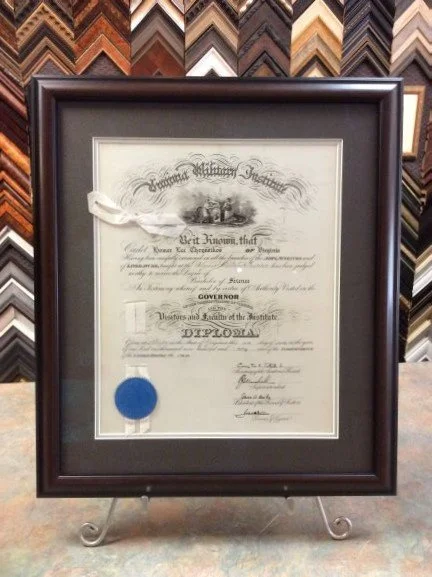 Framed diploma certificate with a blue seal, displayed on a stand, with a colorful frame sample background.