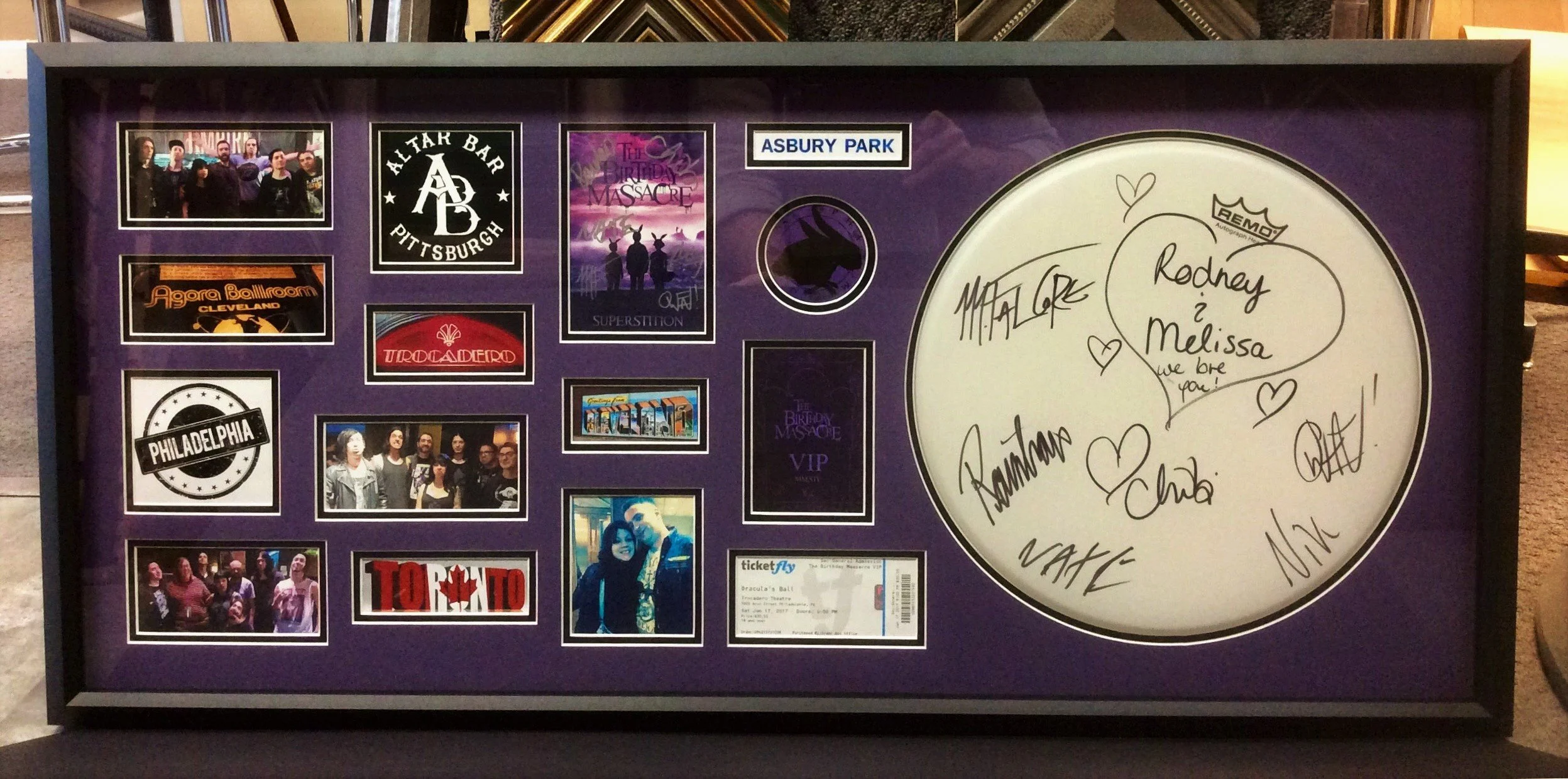 A framed collage of photos, stickers, and signed messages for a music or theater event, with a large white circular autograph area on the right side containing signatures and handwritten notes.