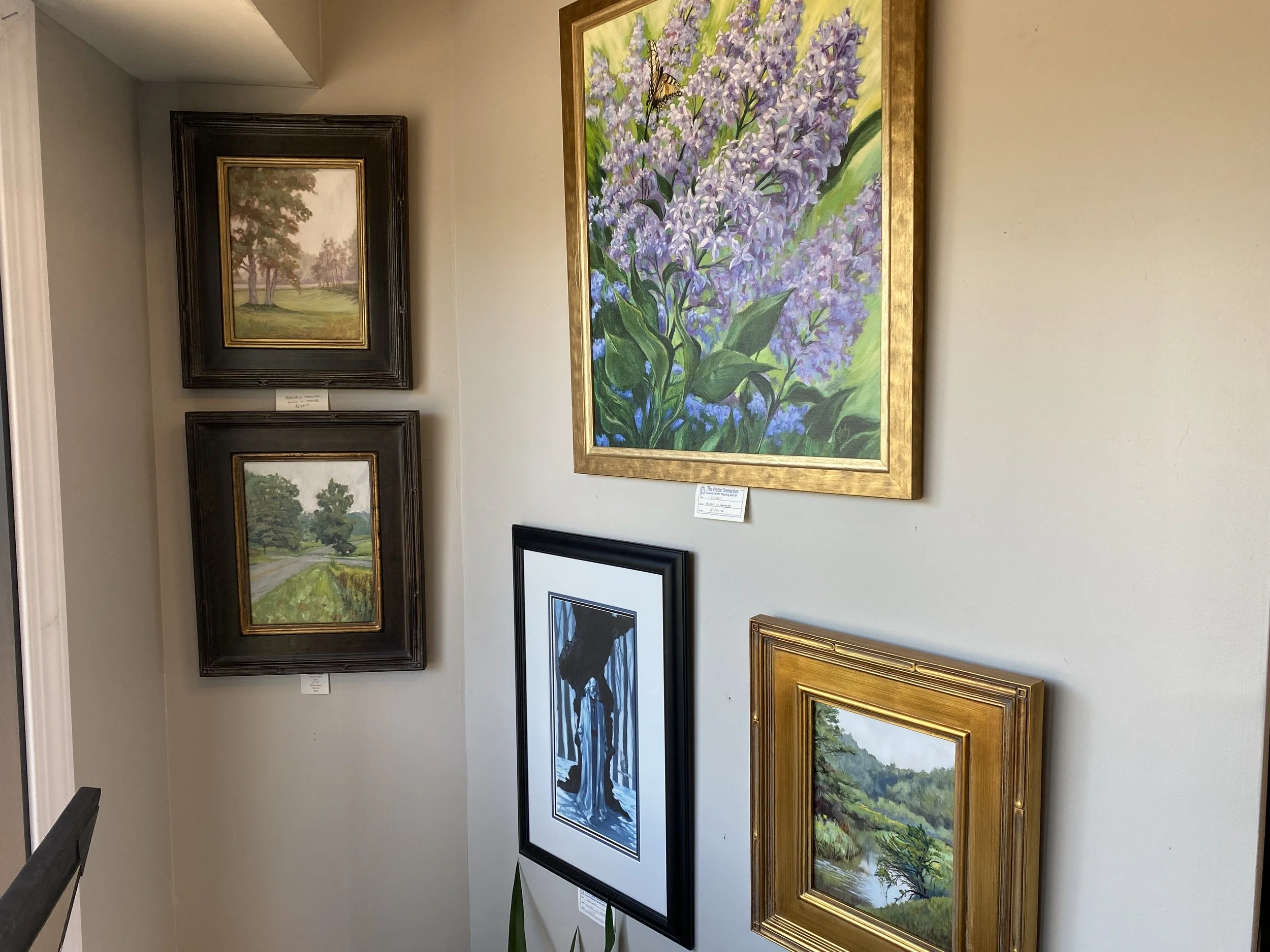 Gallery corner with beige walls displaying various paintings of landscapes, flowers, and figures.
