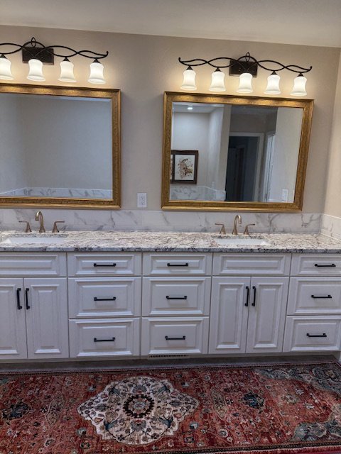 Bathroom vanity with two sinks, marble countertop, large gold-framed mirrors, and multiple light fixtures above each mirror. There is a red patterned rug on the floor. Expert custom mirror framing in Salem, VA, and near Roanoke, VA.
