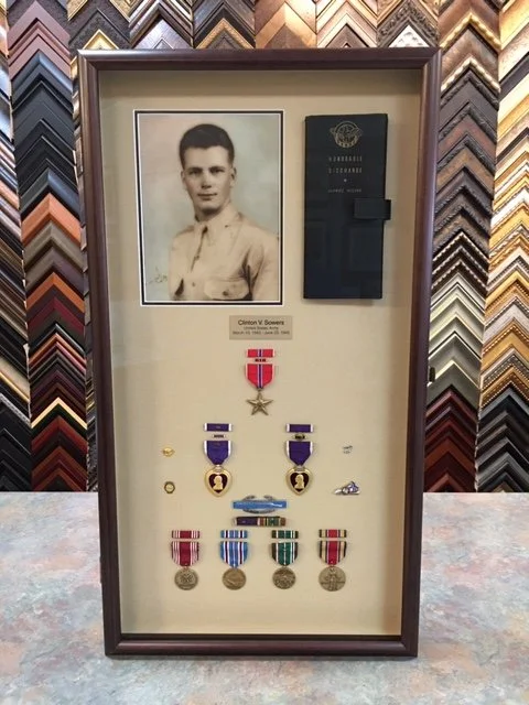 Display case with a black-and-white photograph of a young man in military uniform, a plaque reading "Clinton V. Owens," a document case, a medal, and five military medals with ribbons.