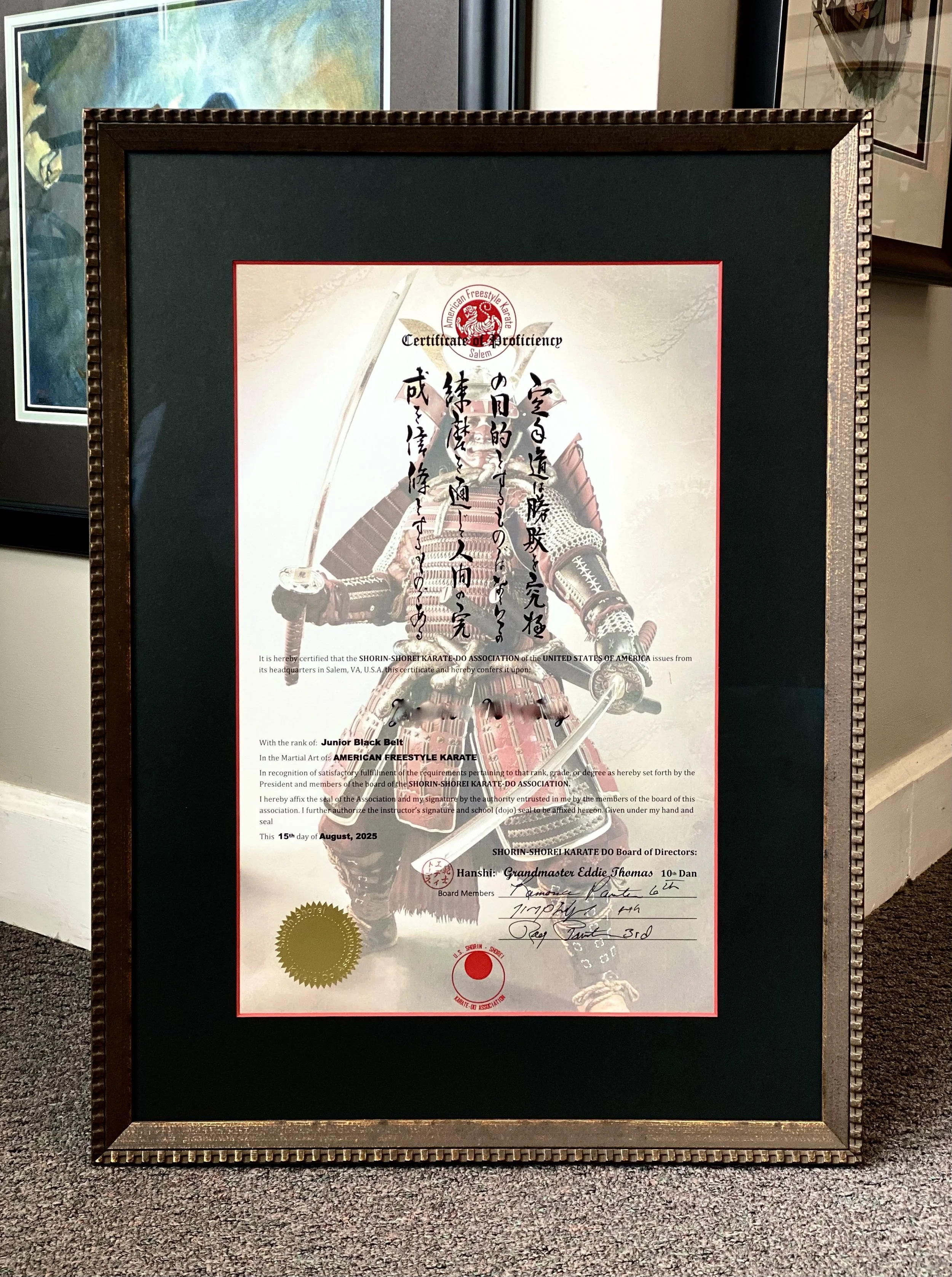 Framed karate certificate with Japanese calligraphy, featuring an image of a samurai warrior in armor, certificates seals, and signatures, displayed on a stand.