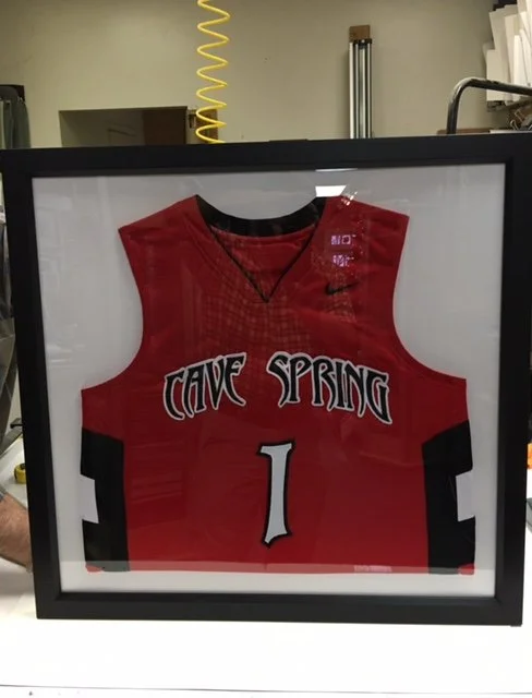 A framed red basketball jersey with black and white accents, displaying the text 'CAVE SPRING' and the number 1.