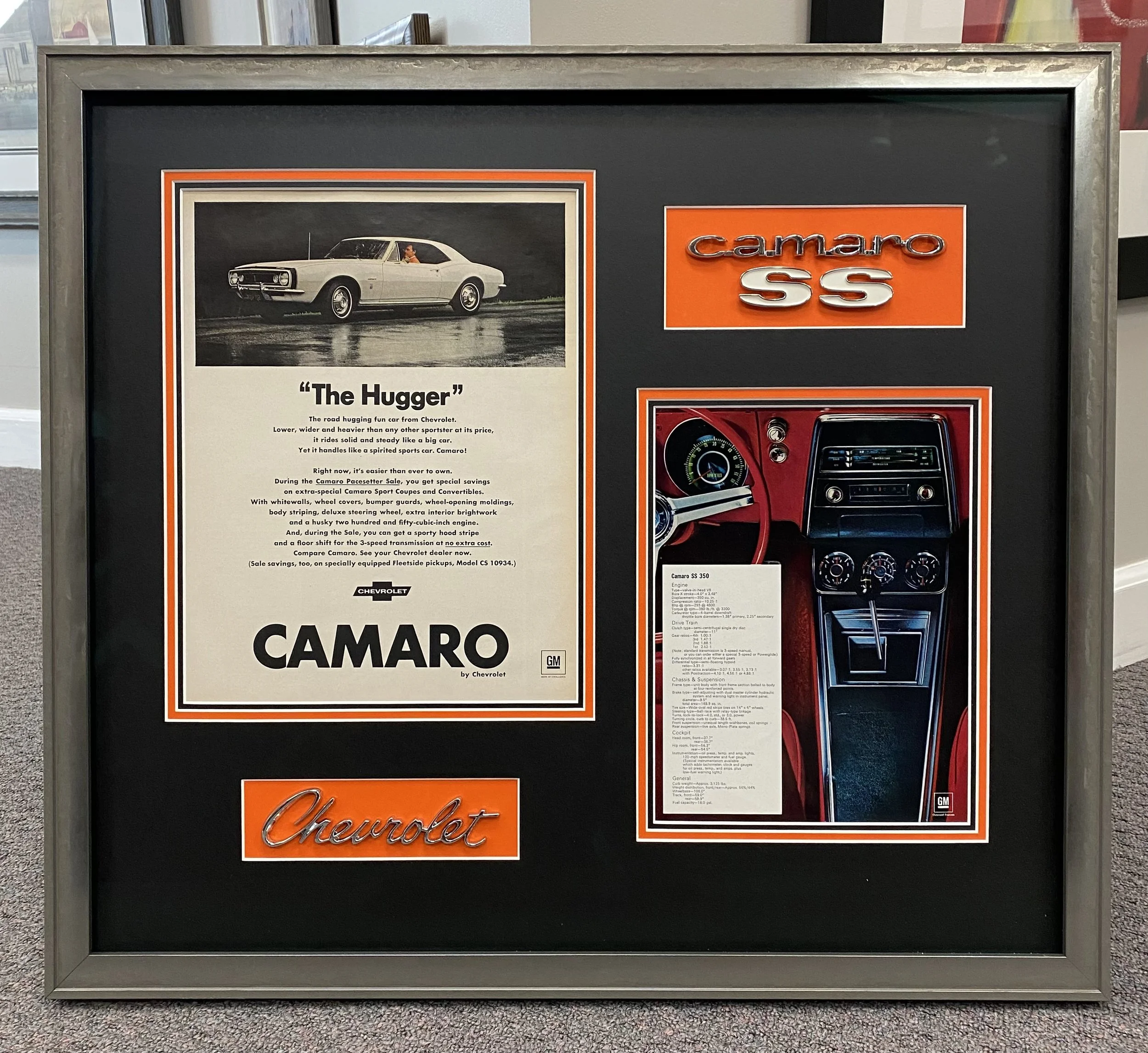 A display board featuring a vintage black and white advertisement for the Chevrolet Camaro, showing a classic coupe car with the text 'The Hugger', and the Chevrolet Camaro logo with orange accents.
