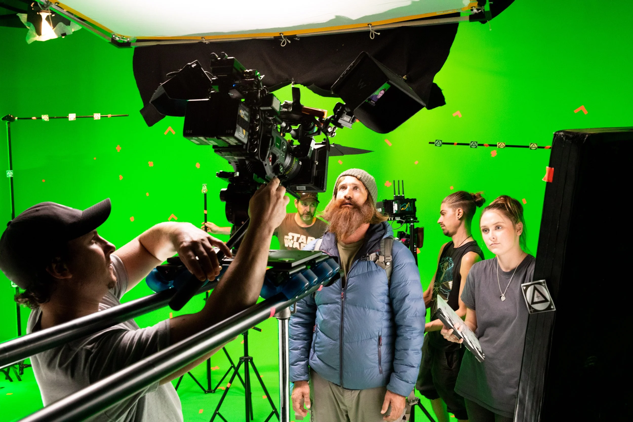 Filming crew setting up on a green screen studio with actors, cameras, and lighting equipment.