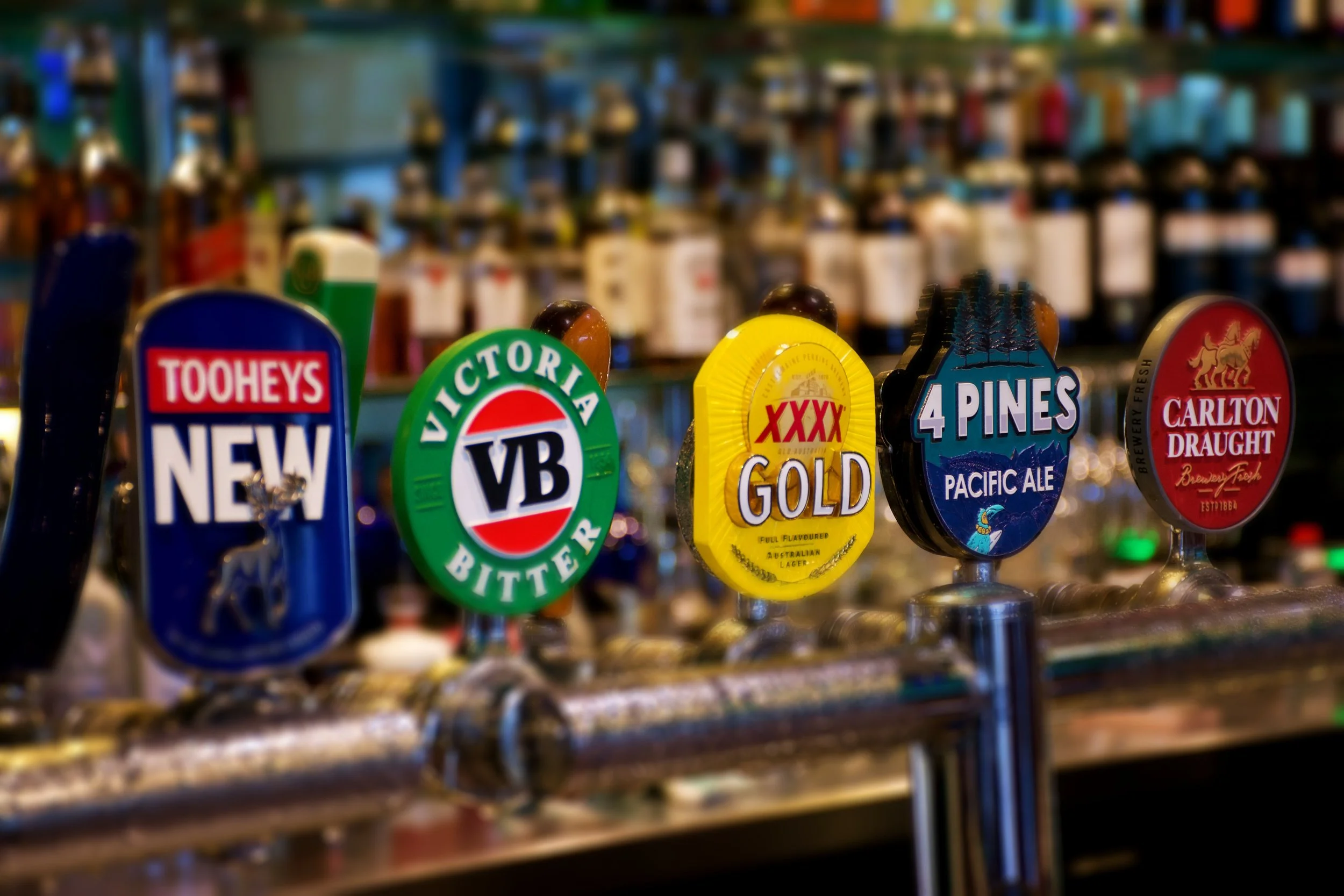 Beer tap handles with brands like Tooheys New, Victoria Bitter, XXXX Gold, 4 Pines Pacific Ale, and Carlton Draught at a bar.