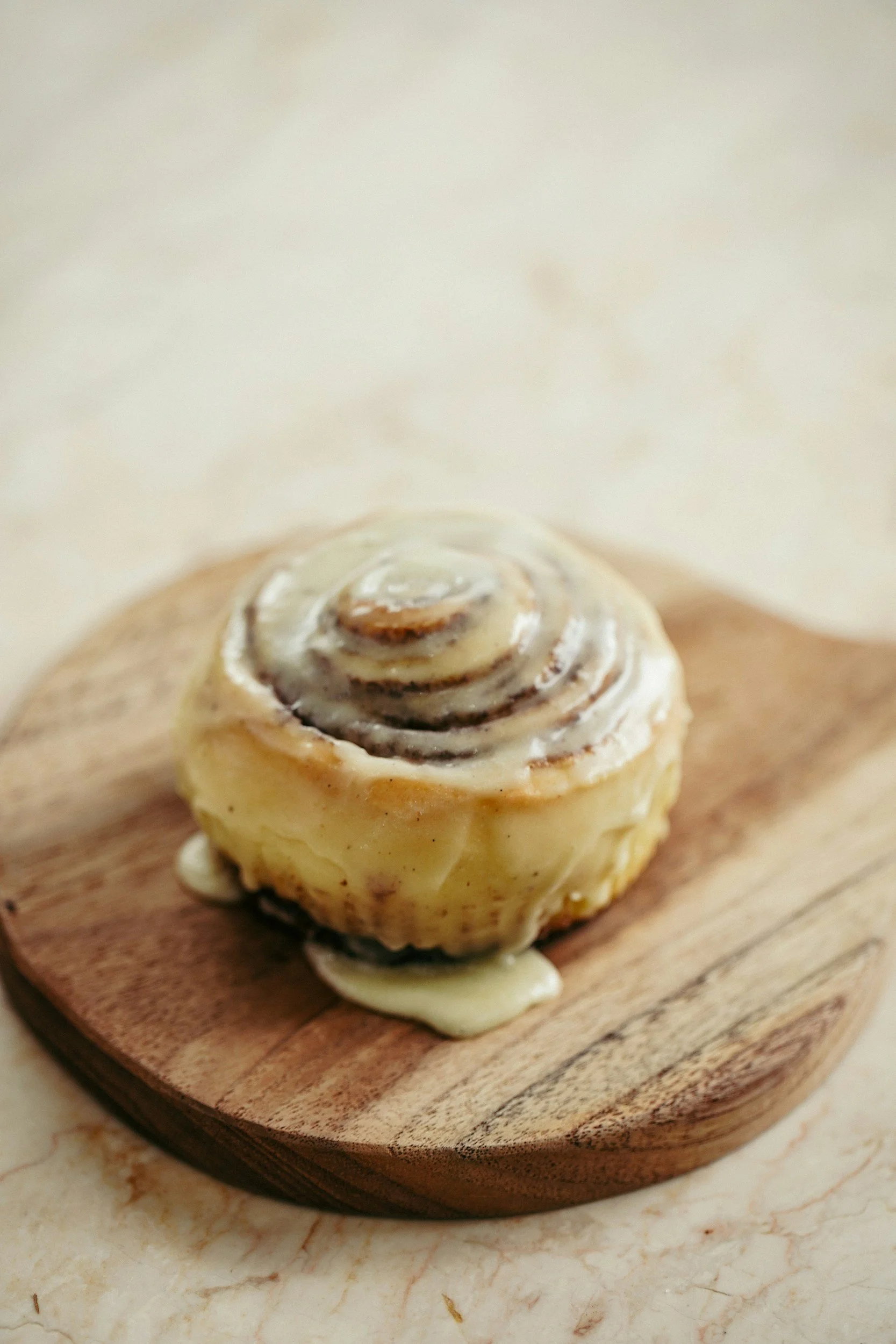 A cinnamon roll drizzled with icing on a wooden cutting board.