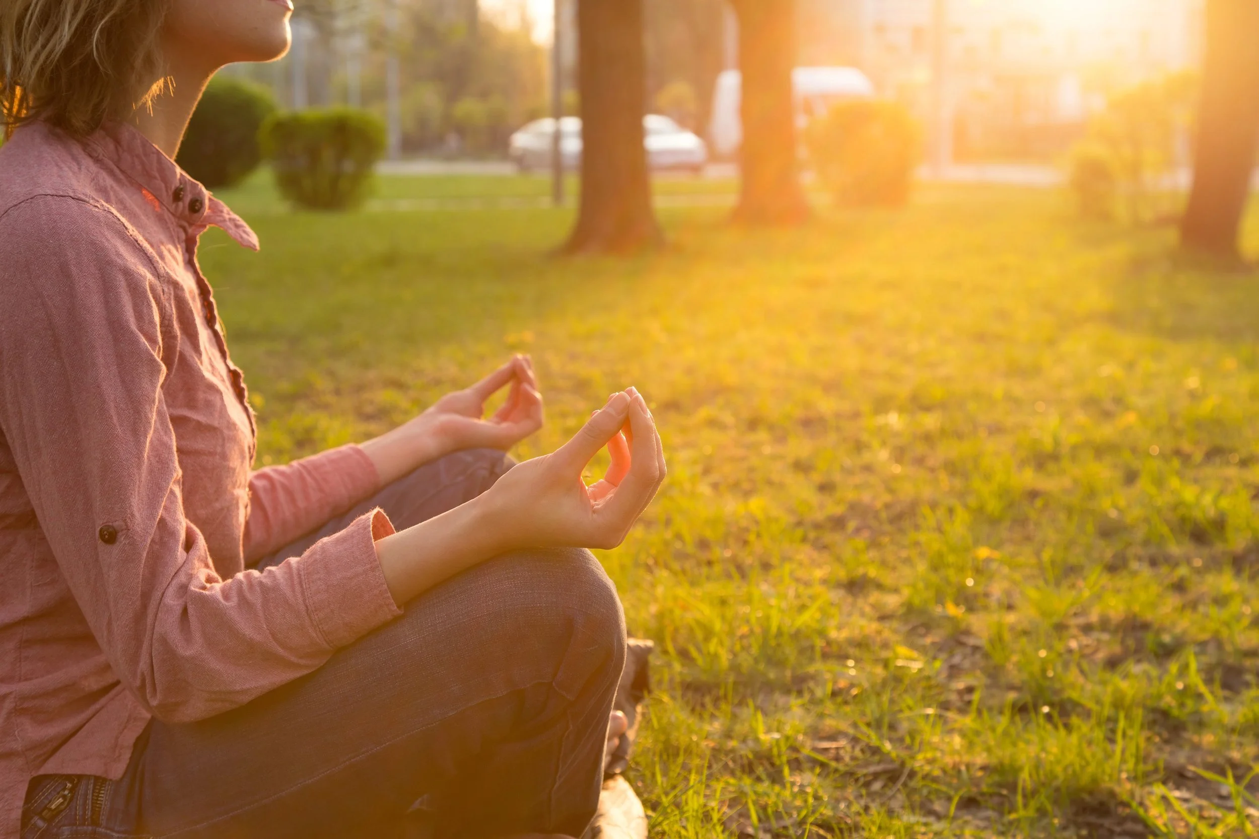 woman sitting cross legged on grass with a meditative hand gesture