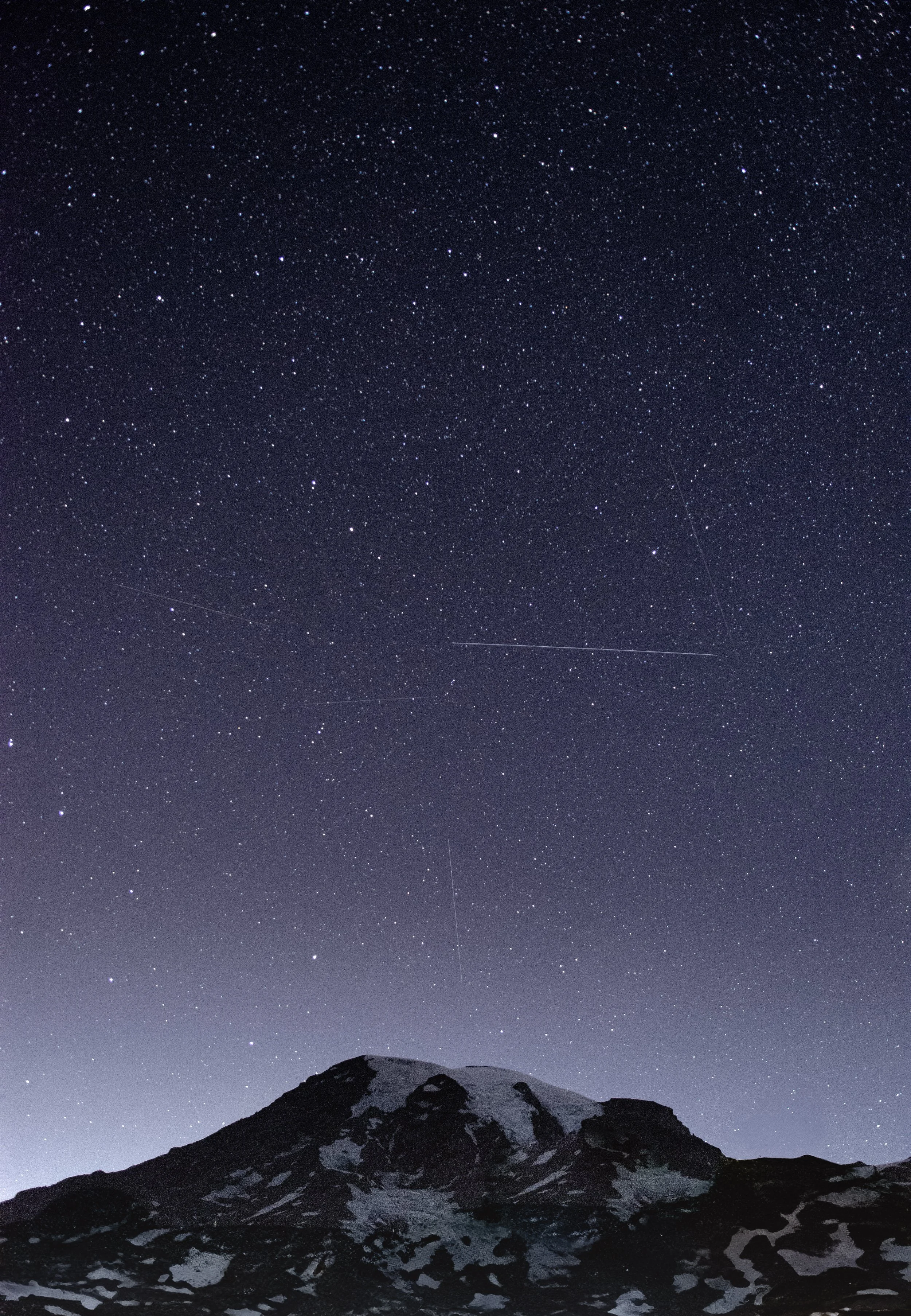Nighttime mountain landscape with a snow-capped peak under a clear, star-filled sky.