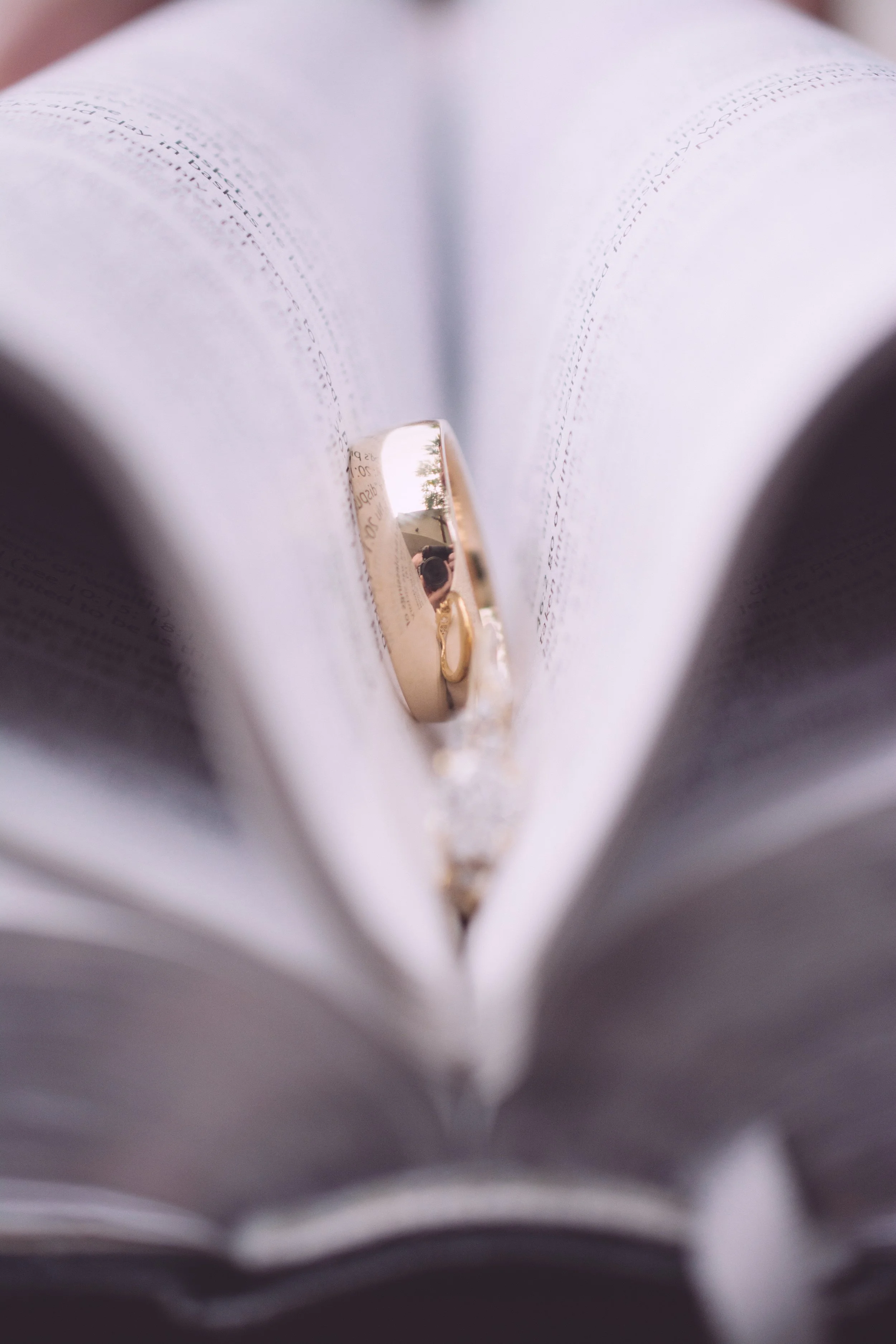 Close-up of open book with a gold wedding ring placed in the center of the pages reflecting surroundings.