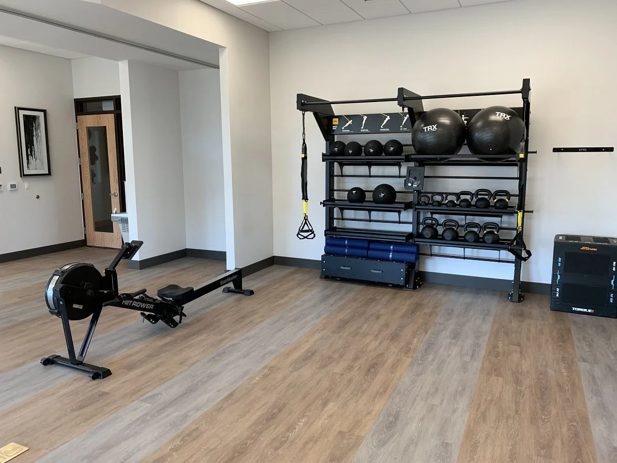 Empty home gym with rowing machine and black workout equipment on wall shelves.