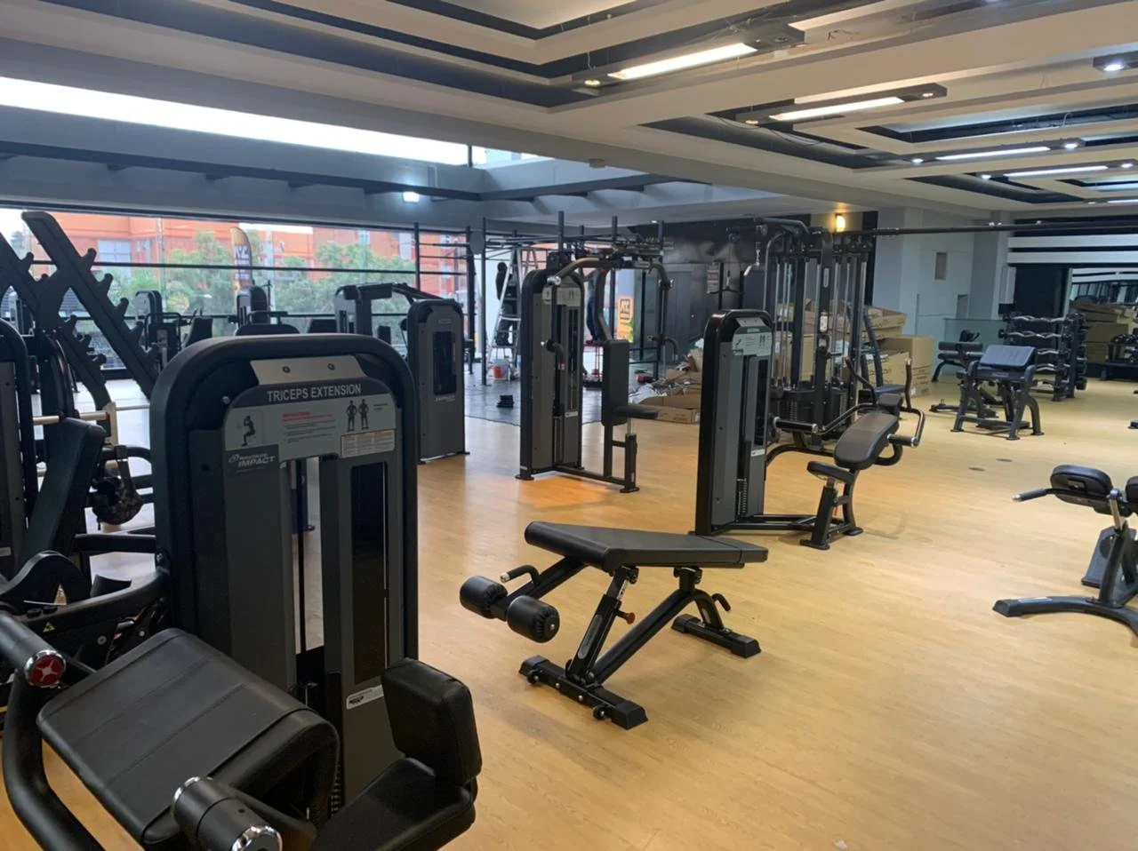 Interior of a modern gym with various workout equipment including benches, weight machines, and cardio equipment, with large windows letting in natural light.