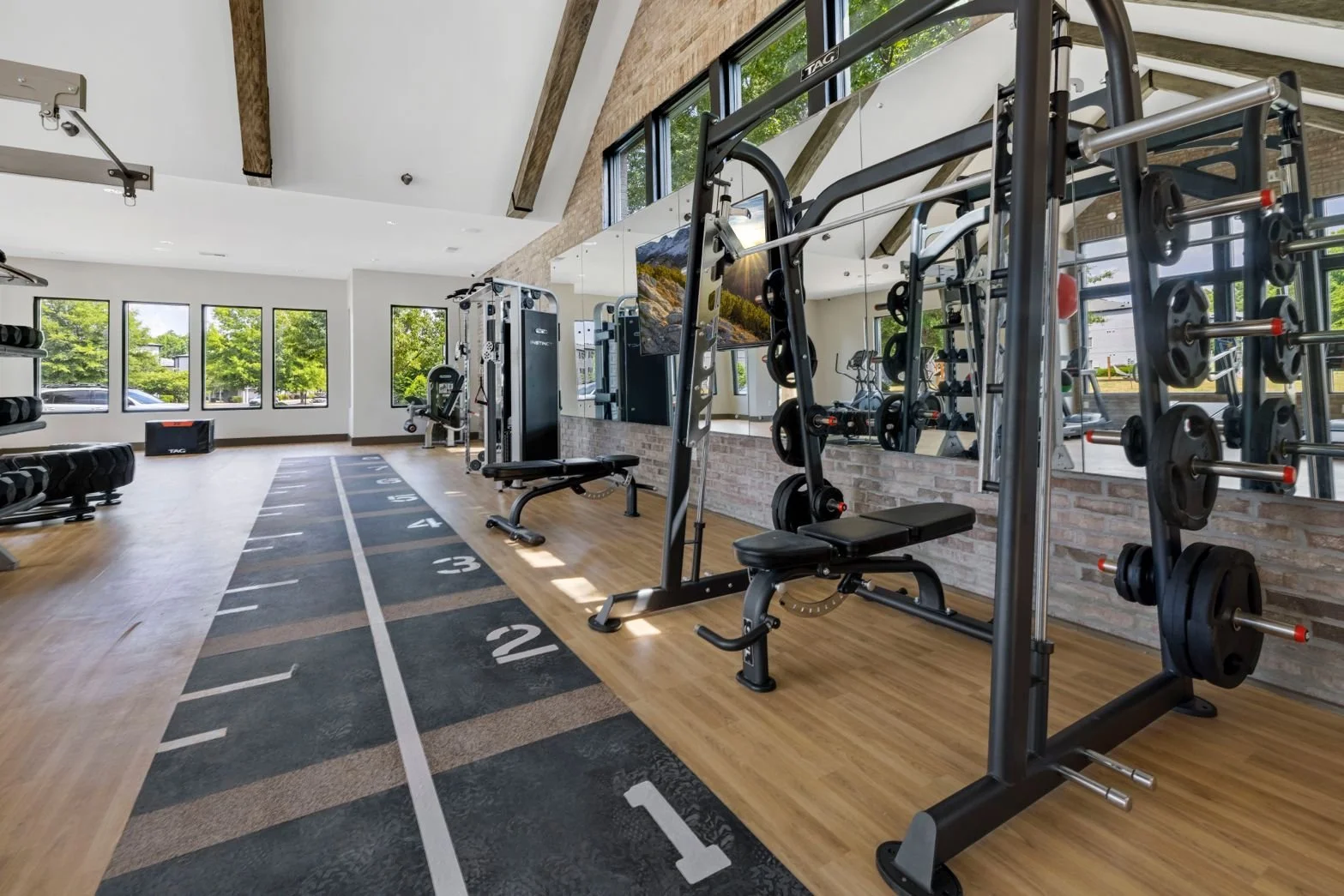 Modern gym with weightlifting equipment, running track, and large windows showing greenery outside.