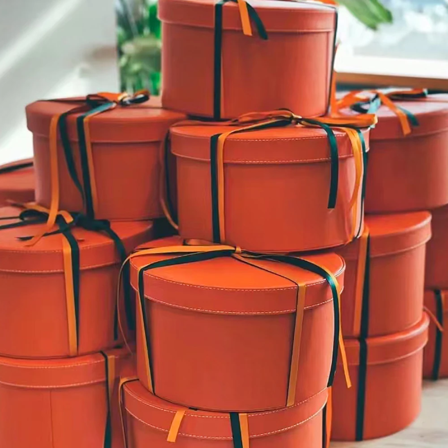 Multiple stacked round orange gift boxes with black and orange ribbons.