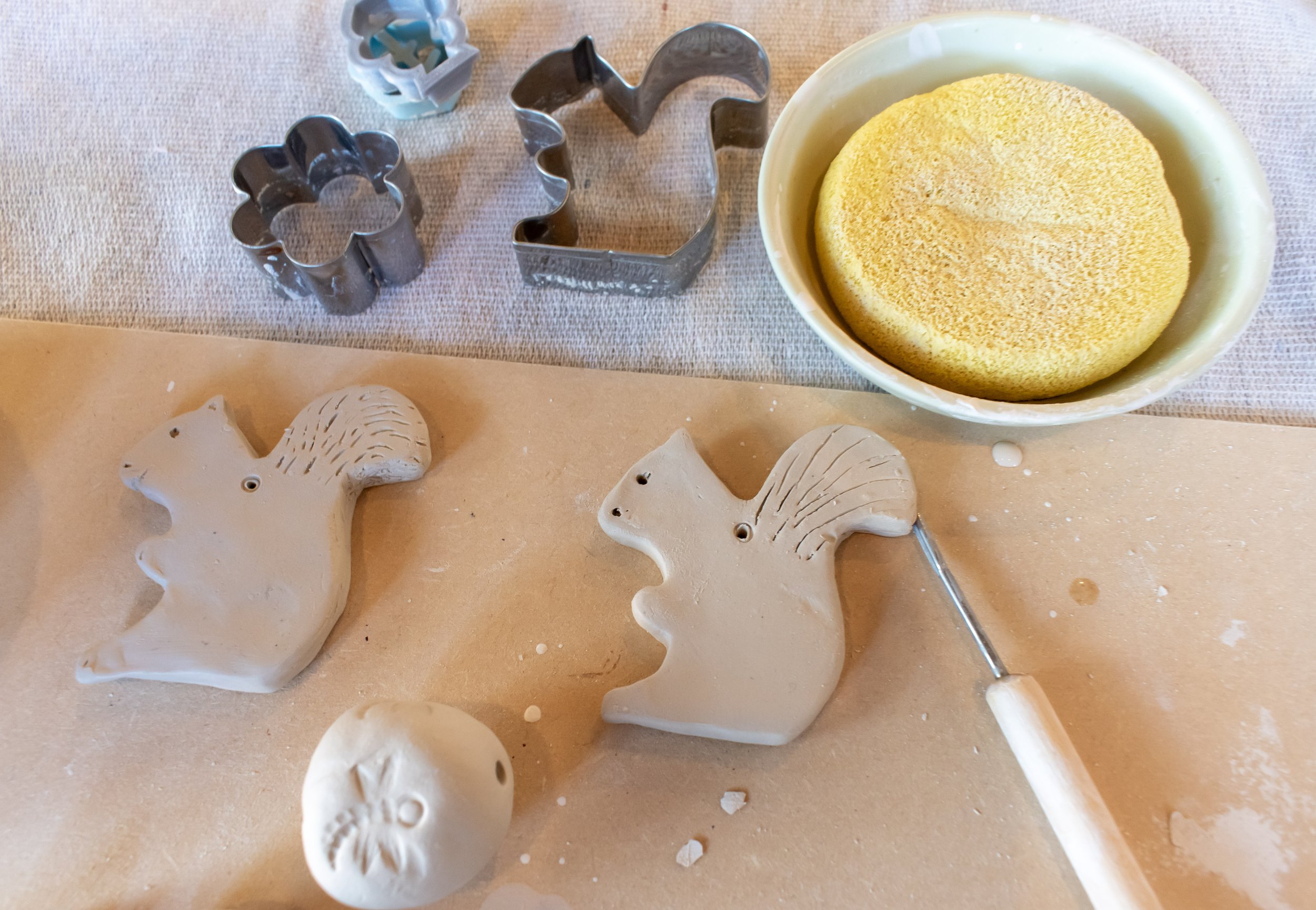 Baking tools and materials, including metal cookie cutters, unbaked animal-shaped cookies, and a bowl with cookie dough, on a countertop.