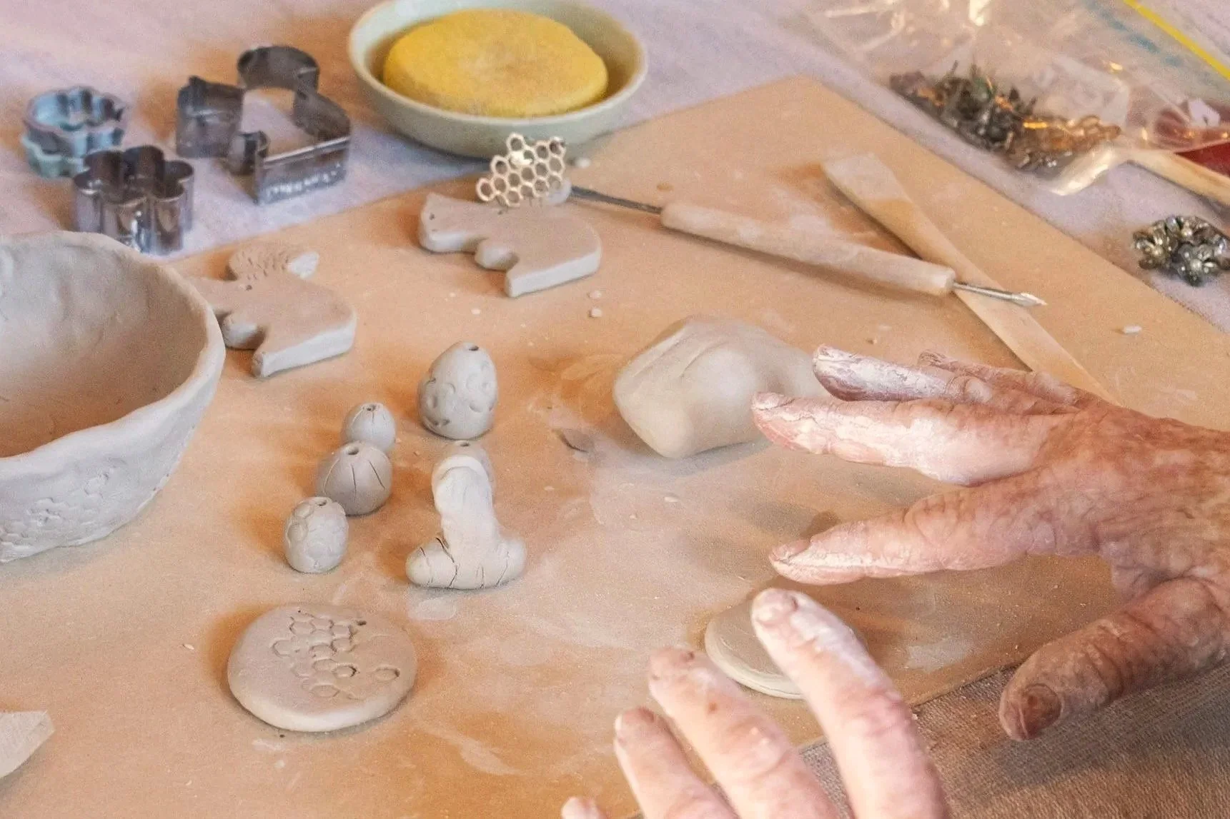 A person working on ceramic pottery, shaping clay with their hands, surrounded by pottery tools, molds, and decorative ceramic pieces on a work surface.