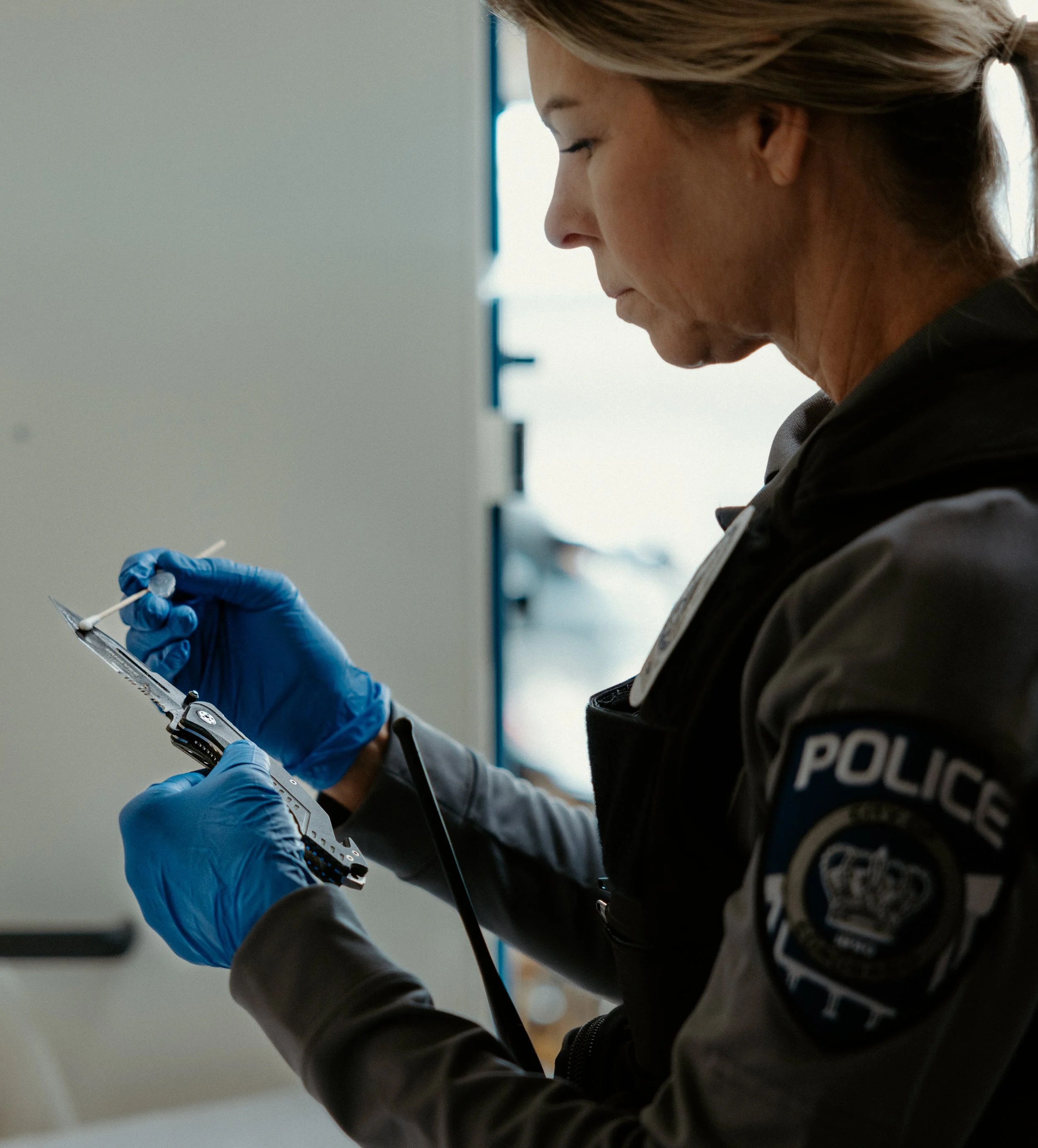 A police officer in uniform and blue gloves is handling a small evidence container and a cotton swab.